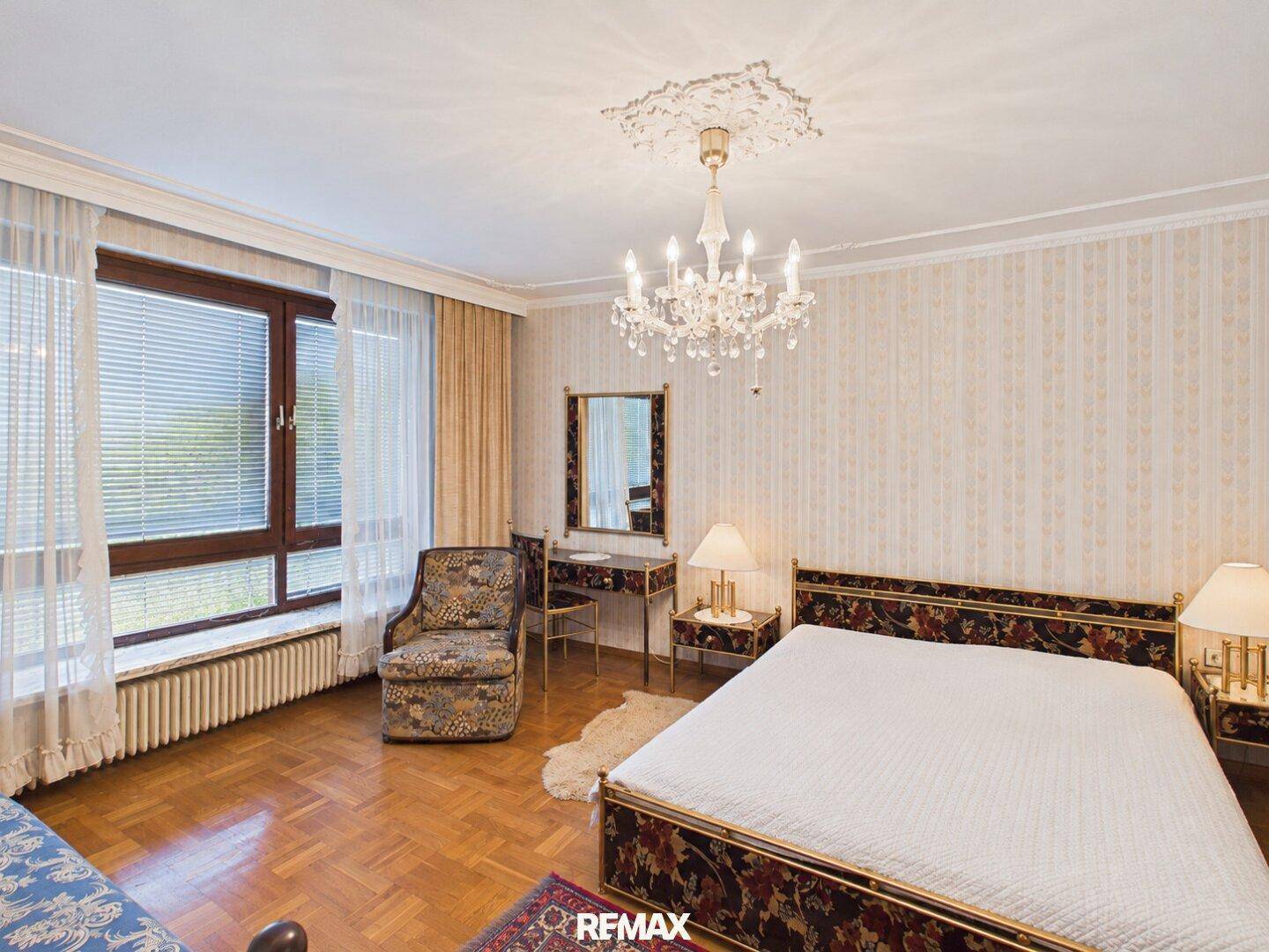 Schlafzimmer mit Parkettboden, gemusterter Tapete und einem Kronleuchter, der eine klassische Atmosphäre schafft.