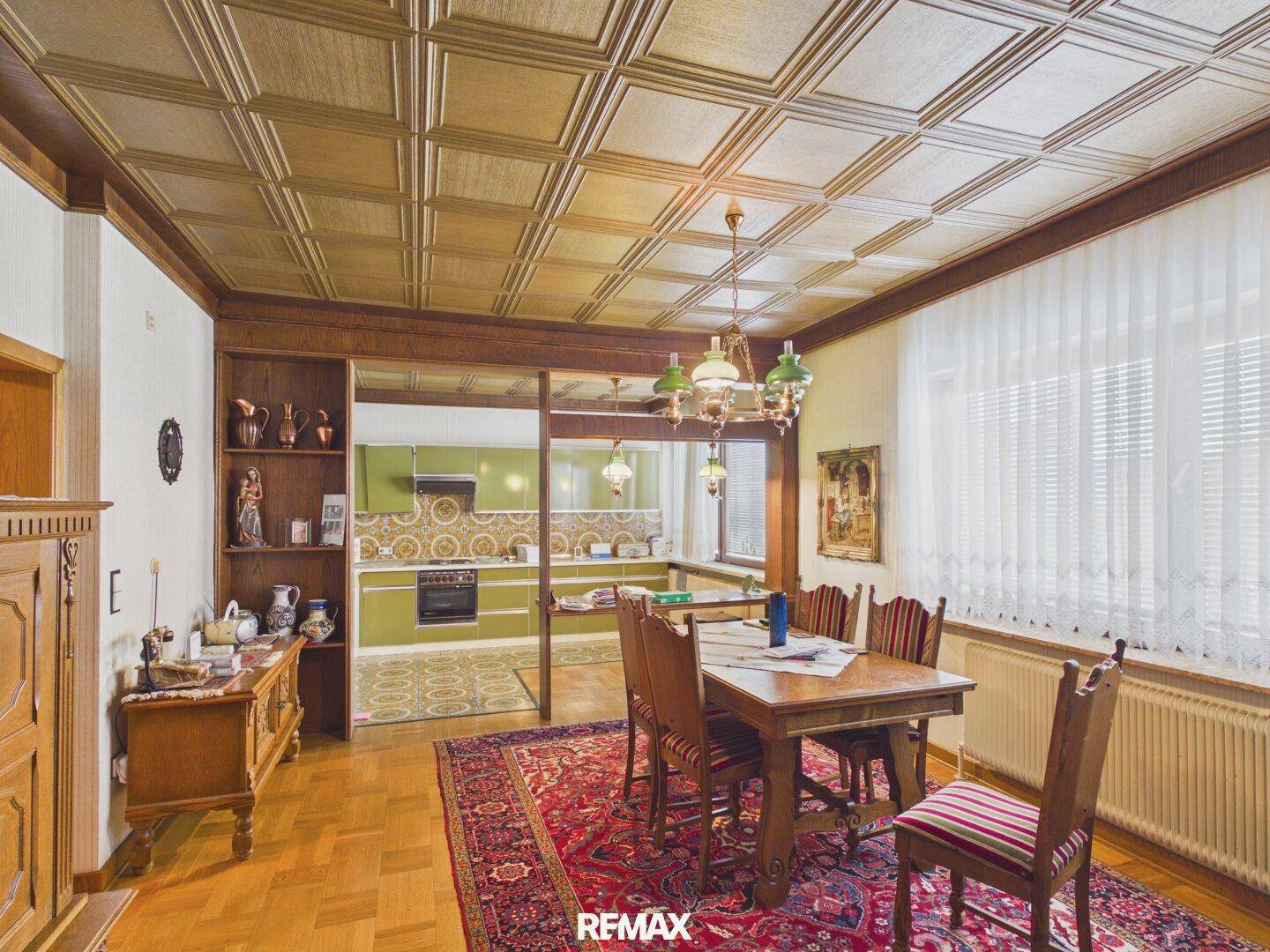 Esszimmer mit Holztisch, Stühlen und einer Decke mit Holzpaneelen, die eine traditionelle Atmosphäre schafft.