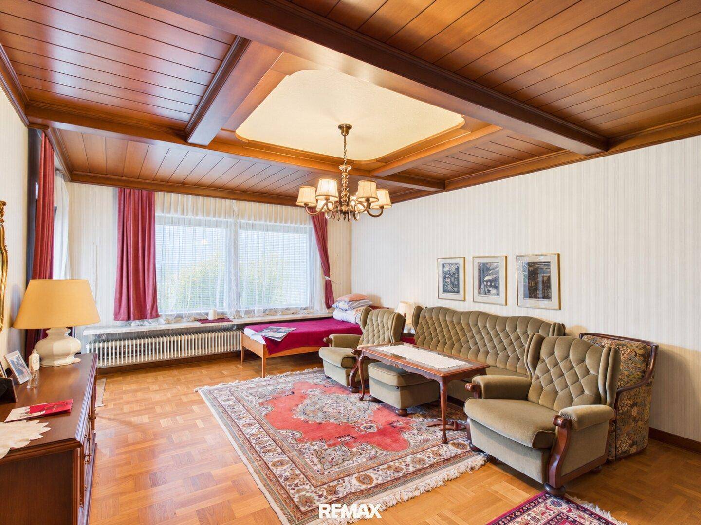 Wohnzimmer mit Parkettboden, gemusterter Tapete und einem Kronleuchter, der den Raum erhellt.