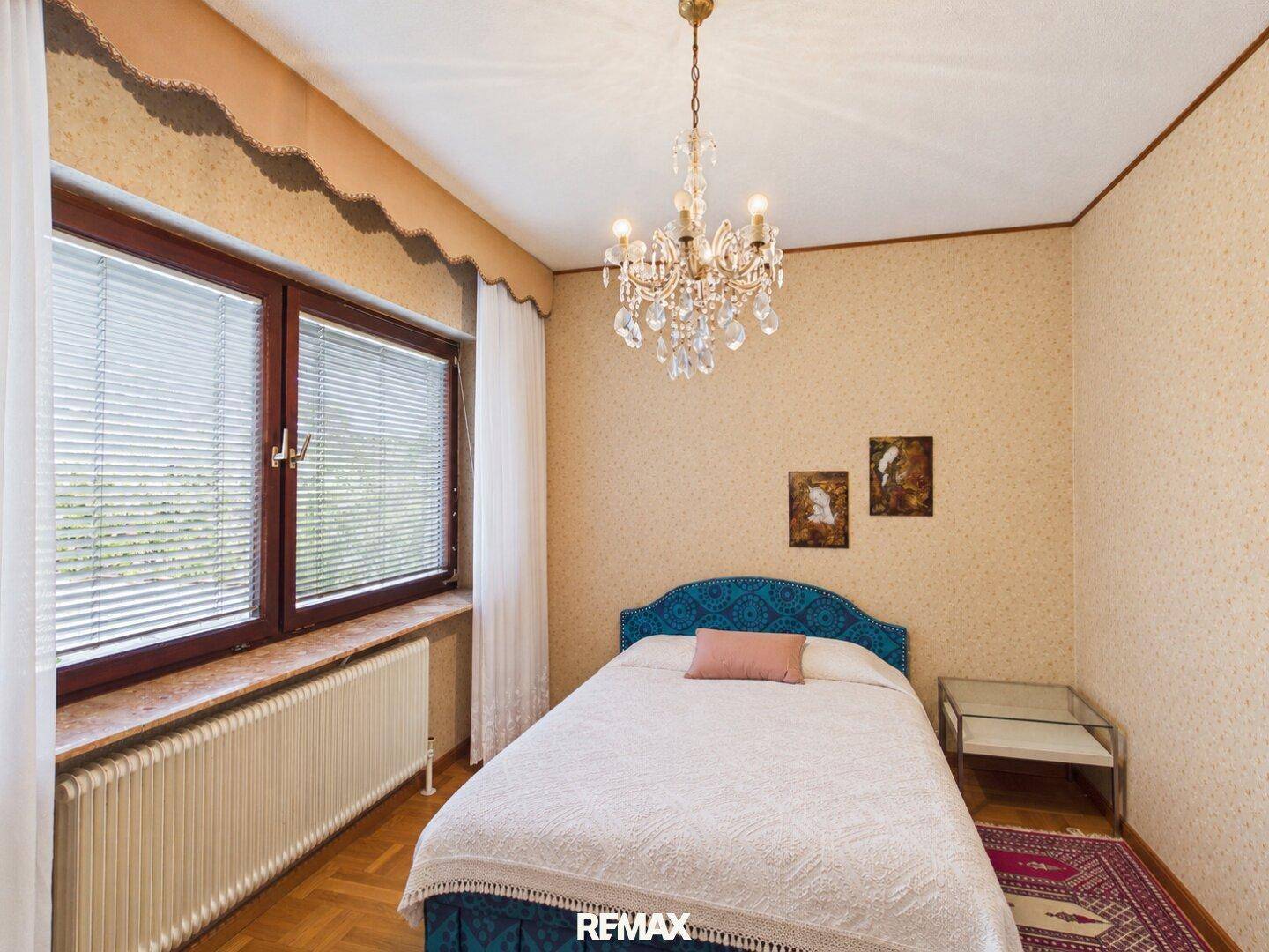 Schlafzimmer mit Parkettboden, gemusterter Tapete und einem blauen Kopfteil, das einen Farbakzent setzt.