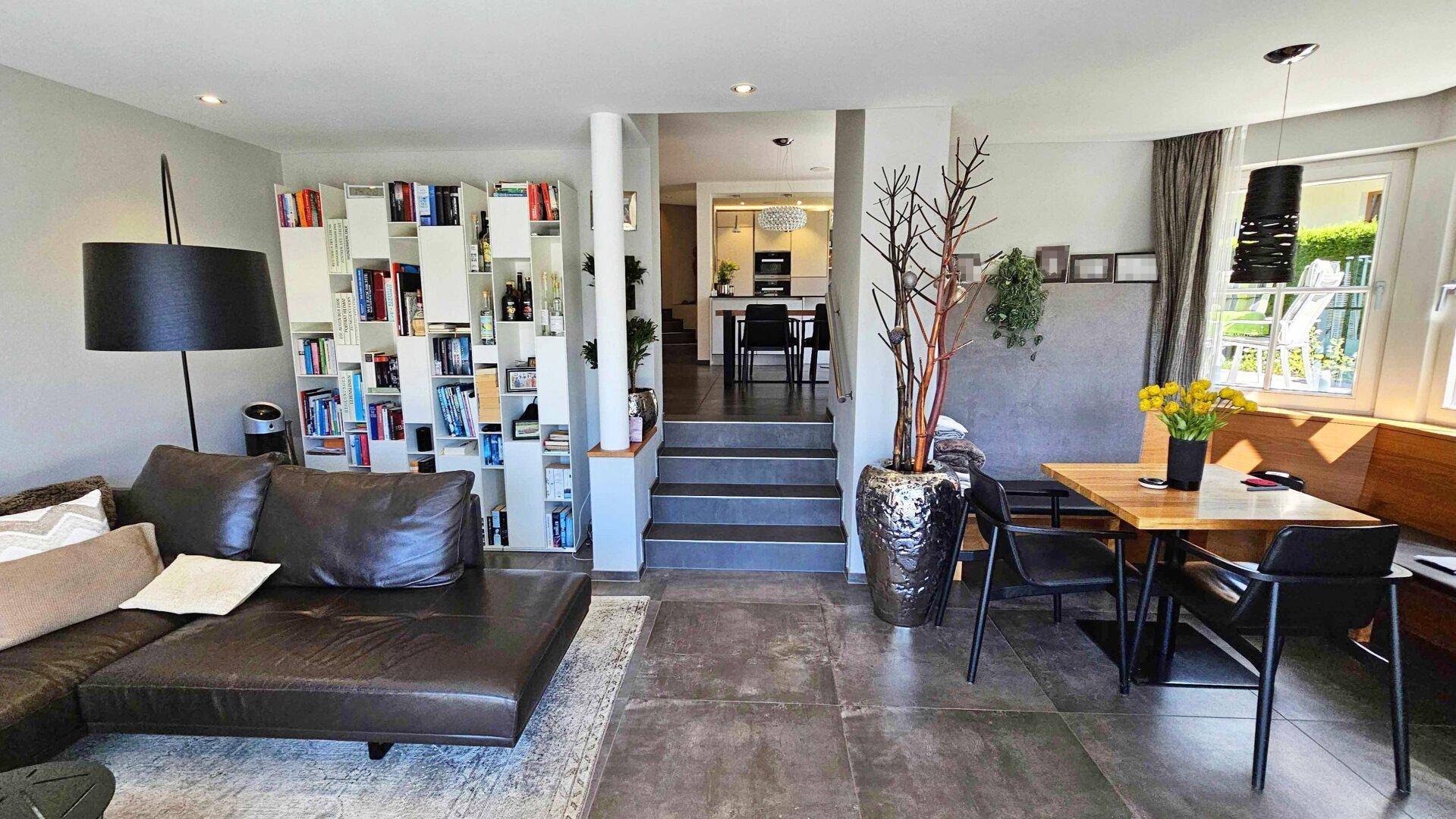 Geräumiges Wohnzimmer mit Ledersofa, Bücherregal und Blick auf den Essbereich.