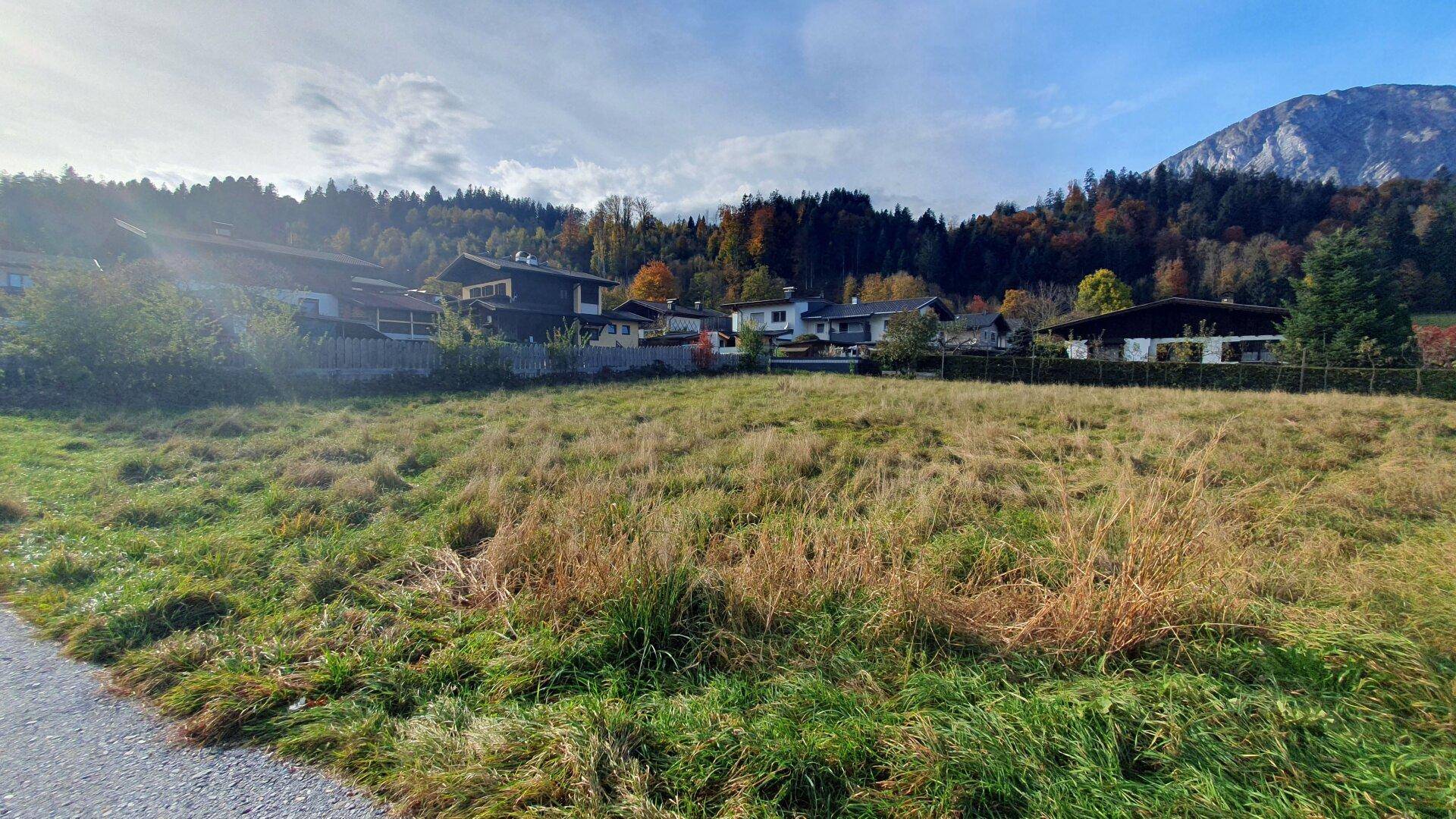 Weitläufiges, grünes Grundstück mit Blick auf die herbstliche Berglandschaft und benachbarte Häuser.