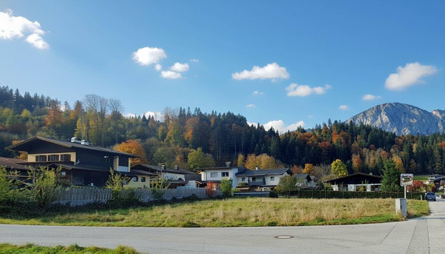 Panoramablick auf ein Wohngebiet mit Herbstbäumen und Bergen unter einem klaren blauen Himmel.