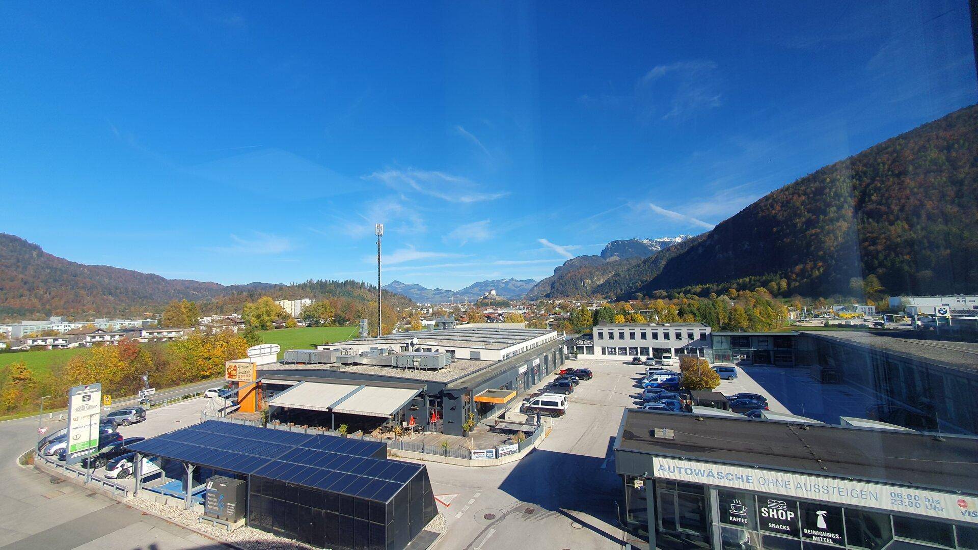 Weitläufiger Ausblick aus dem Fenster auf ein Tal mit Bergen, einer Gewerbefläche und Solaranlagen.