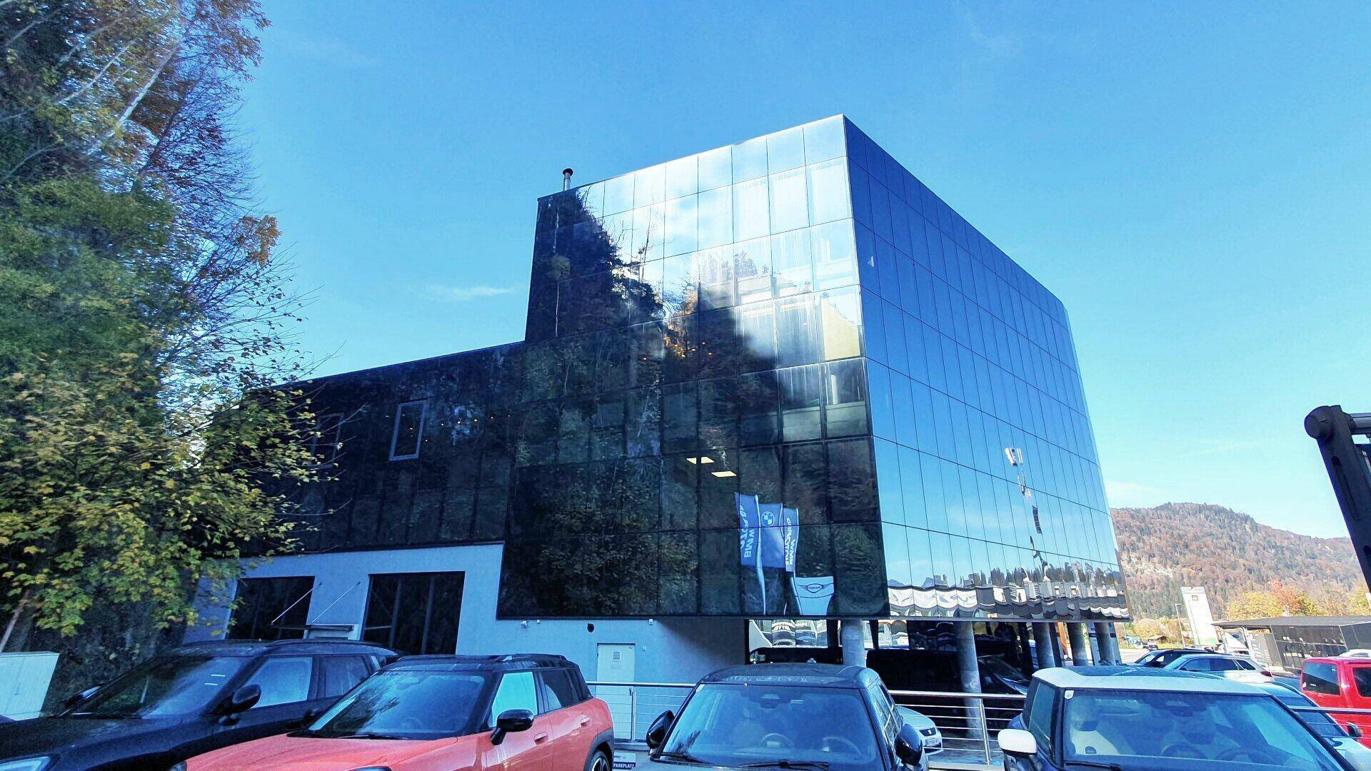 Ansicht der Seitenfassade eines modernen Glasgebäudes mit Bäumen und geparkten Autos im Vordergrund.