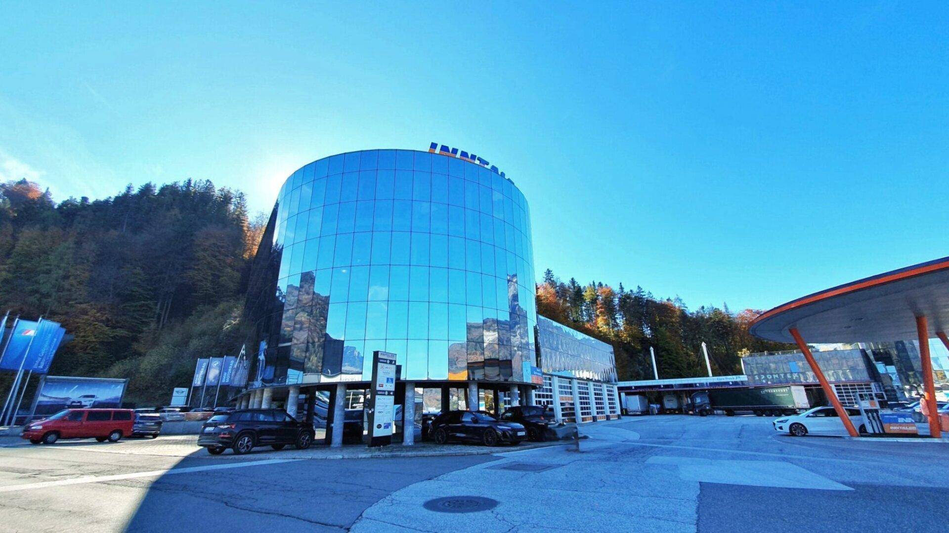 Weitläufige Ansicht eines modernen Gebäudes mit runder Glasfassade und Parkplätzen unter blauem Himmel.
