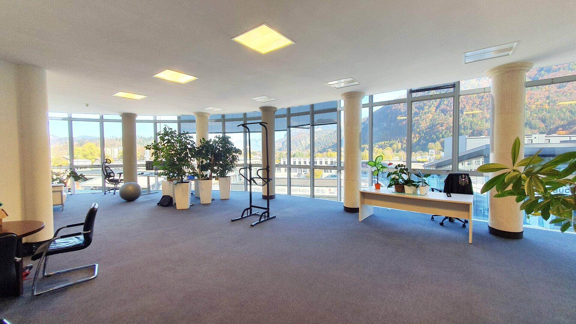 Offener Bürobereich mit großen, gebogenen Fenstern, Teppichboden und Panoramablick auf die Berge.