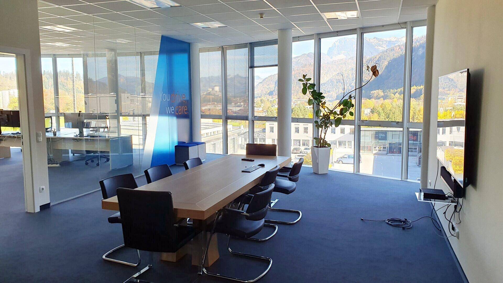 Moderner Konferenzraum mit großem Holztisch, Teppichboden und weitem Blick auf die umliegende Berglandschaft.