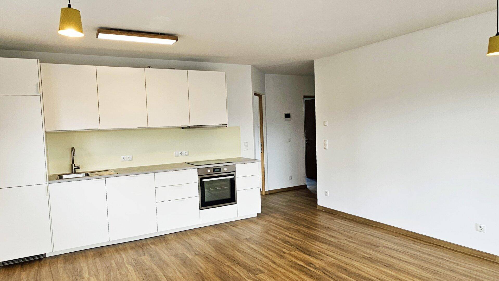 Moderne, offene Küchenzeile mit weißen Schränken, integriertem Backofen und Holzboden.
