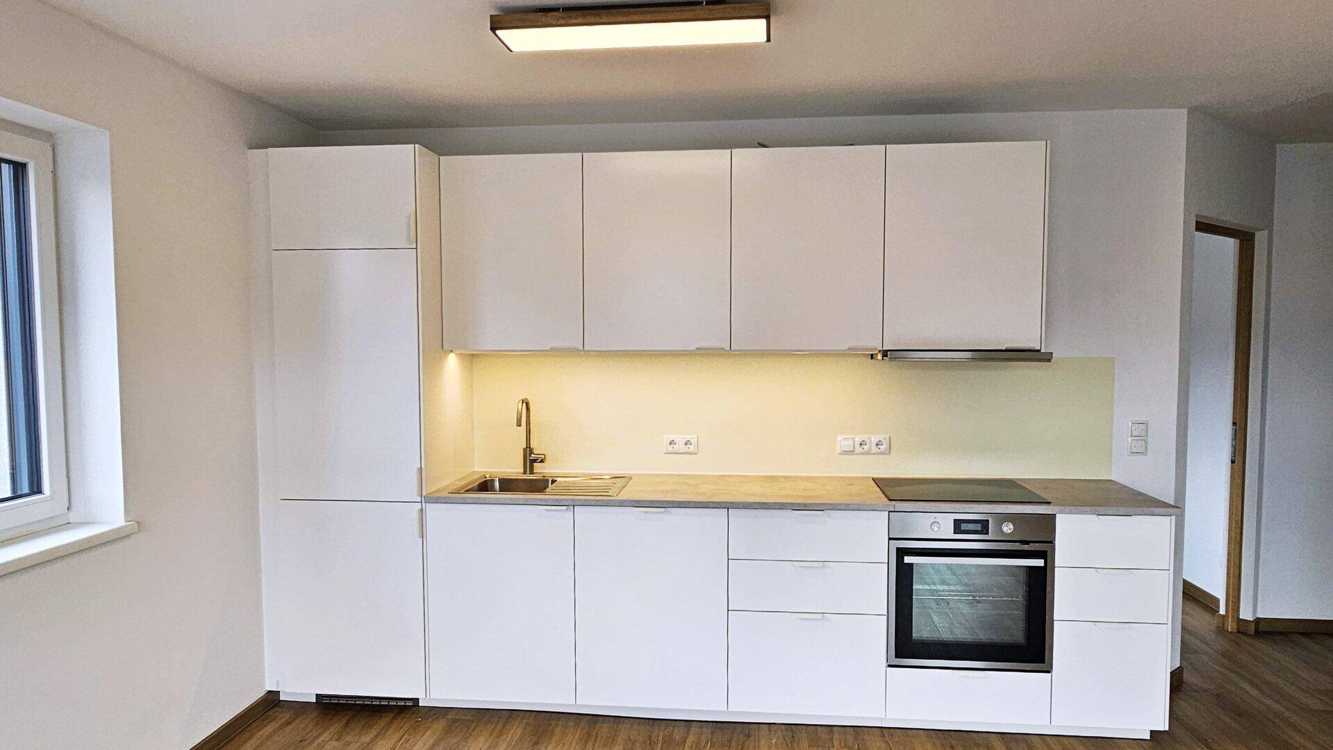 Detailansicht einer modernen weißen Einbauküche mit Spüle, Kochfeld und Backofen.