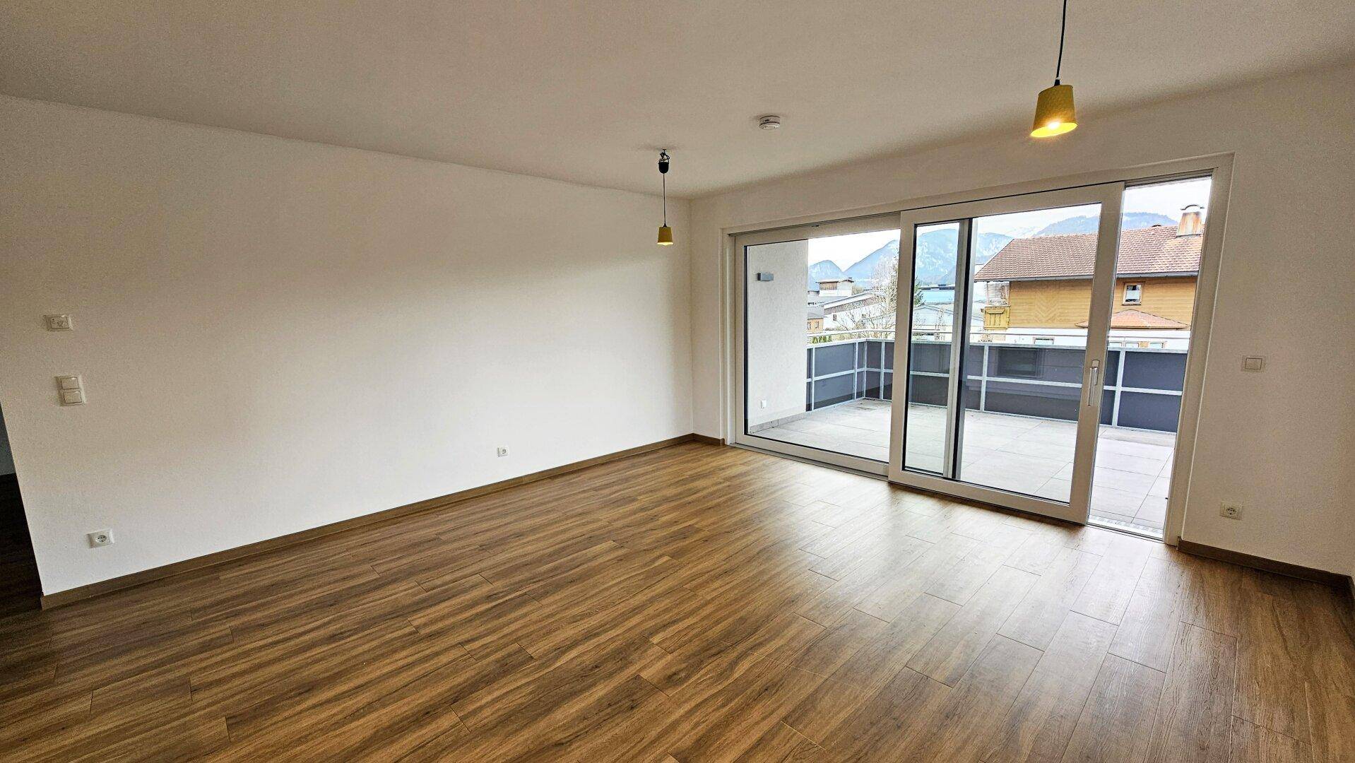 Geräumiger Wohnbereich mit Holzboden und großer Schiebetür, die zu einer Terrasse führt.