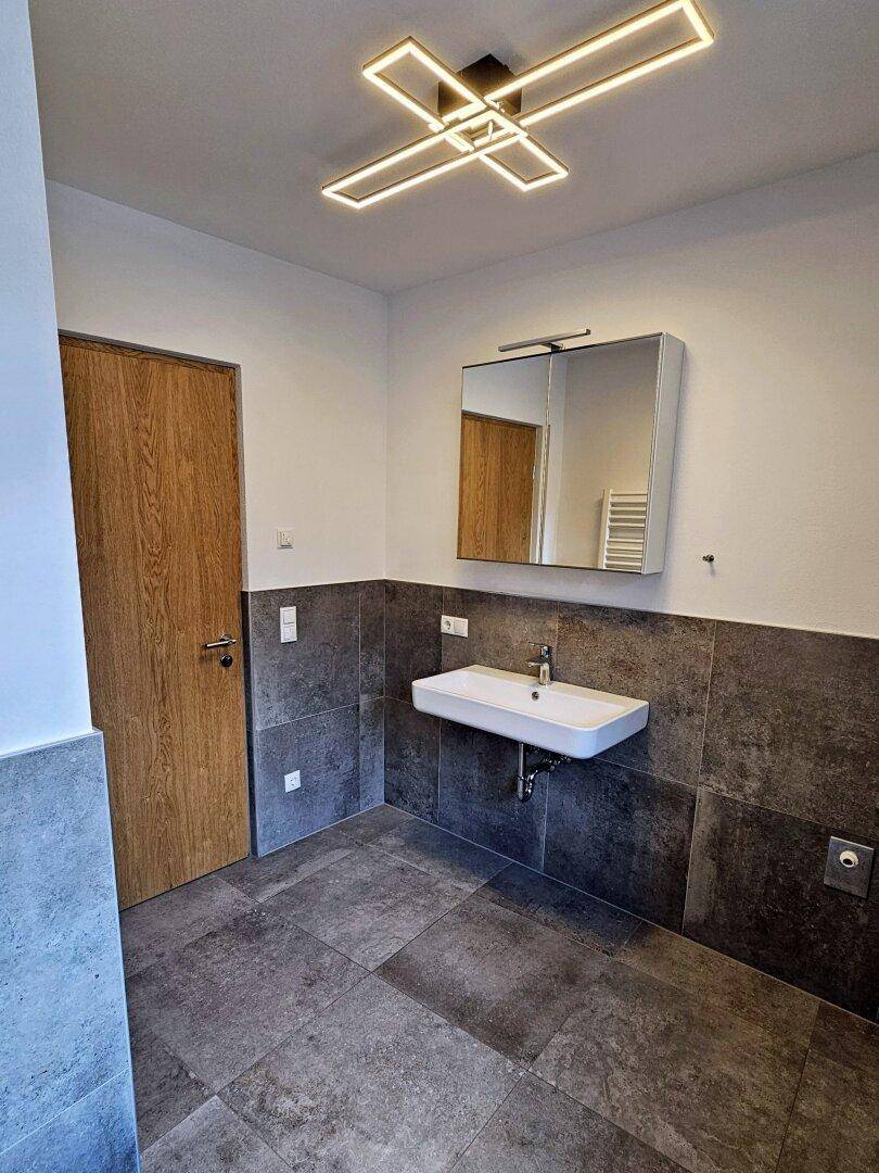 Modernes Badezimmer mit Waschbecken, Spiegelschrank und grauen Wand- und Bodenfliesen.