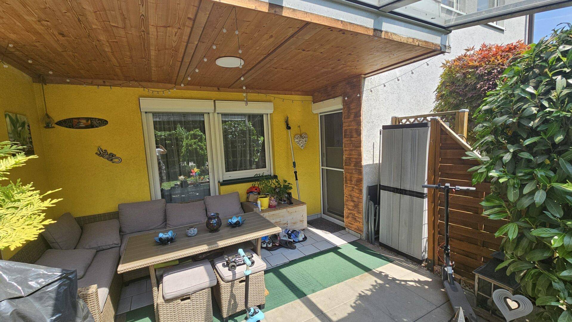 Überdachte Terrasse mit Außenmöbeln, Holzdach und Zugang zum Garten.