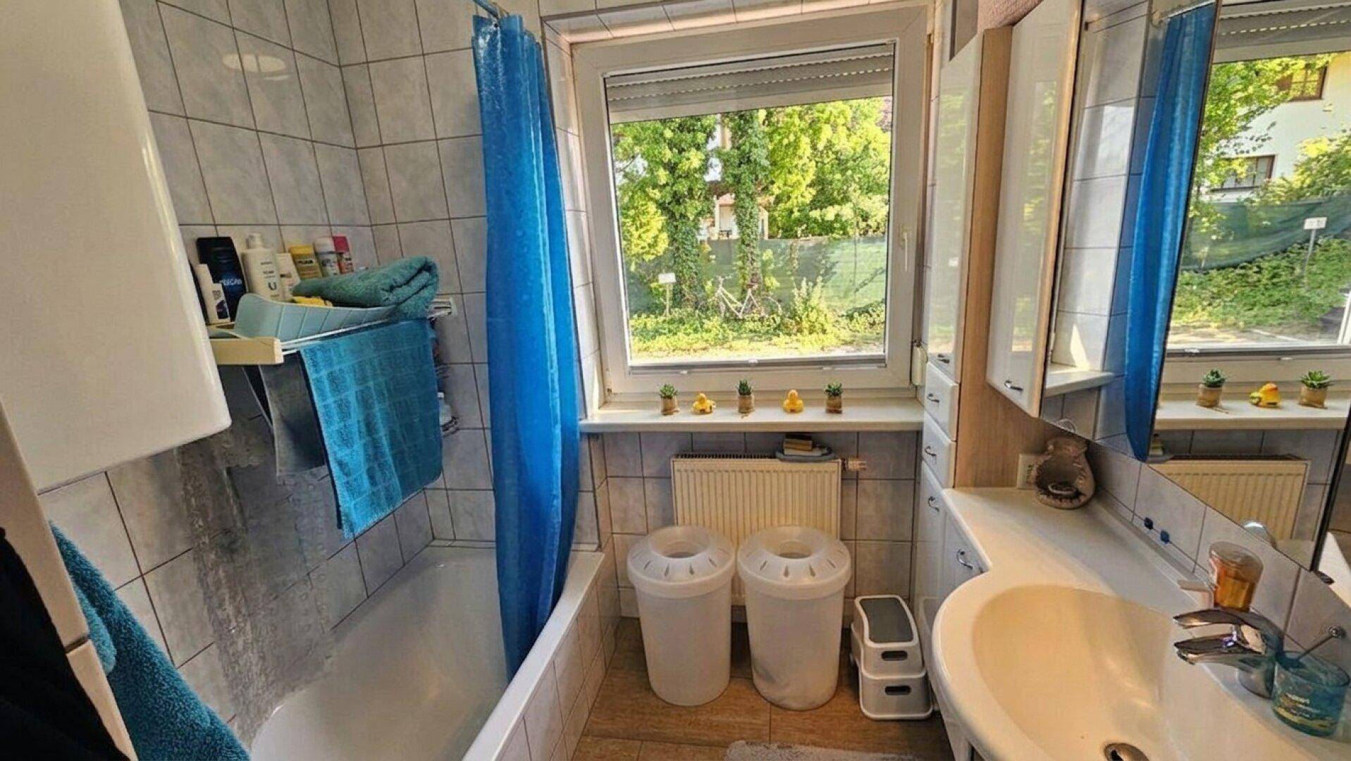 Gefliestes Badezimmer mit Badewanne, Waschbecken und Fenster zum Außenbereich.