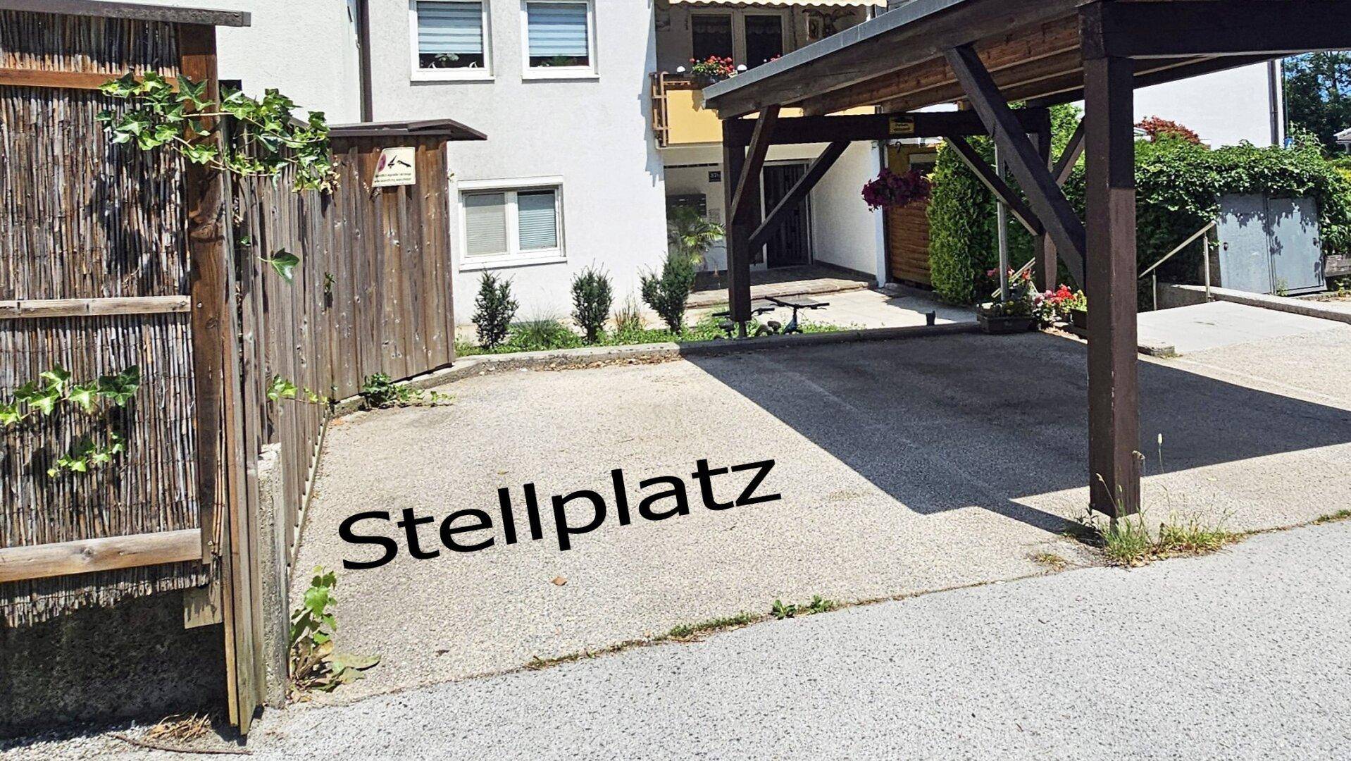 Außenstellplatz mit Carport vor einem Mehrfamilienhaus.