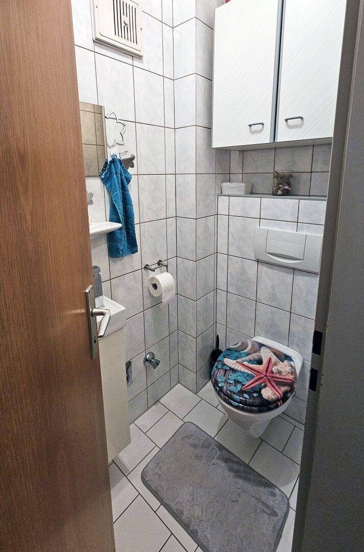 Kleines Gäste-WC mit Wand-WC, Waschbecken und weißen Fliesen.