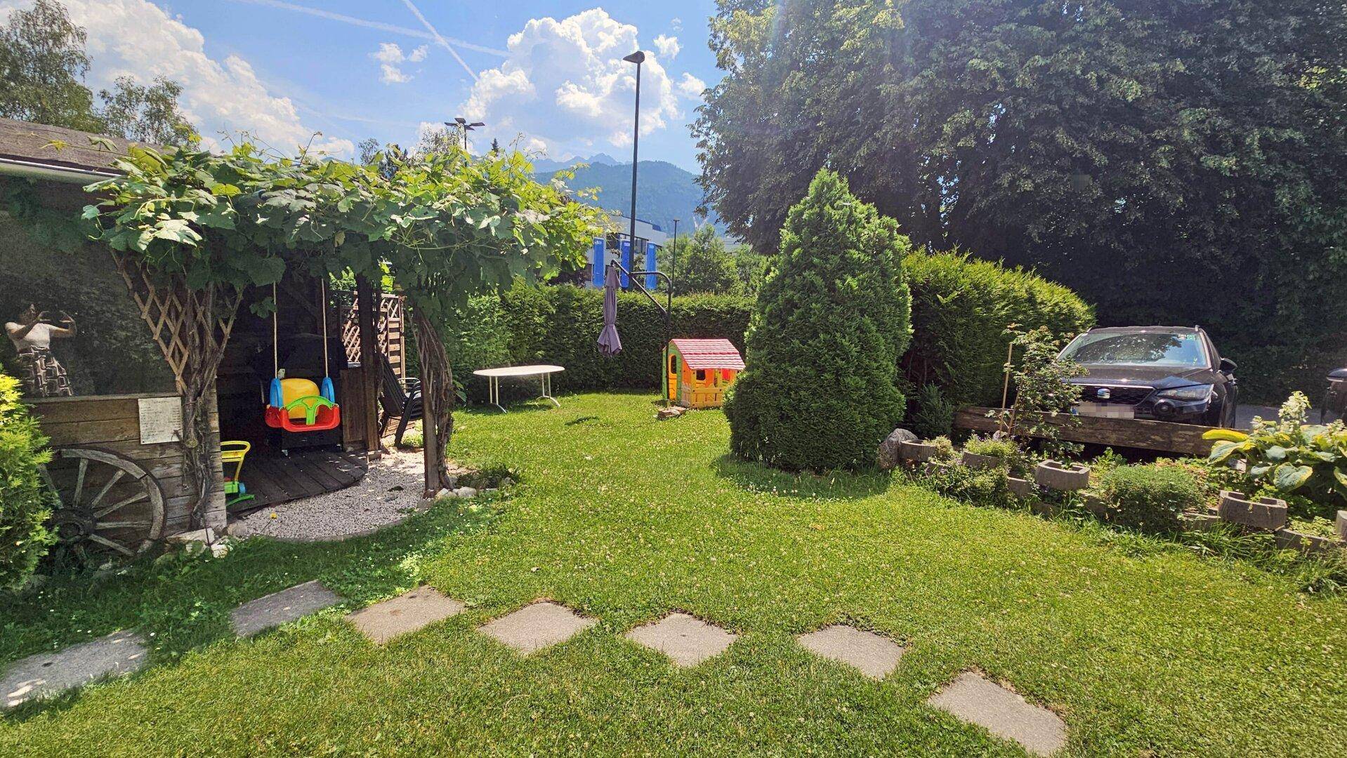 Großer Garten mit Rasenfläche, Schaukel und Spielhaus für Kinder.