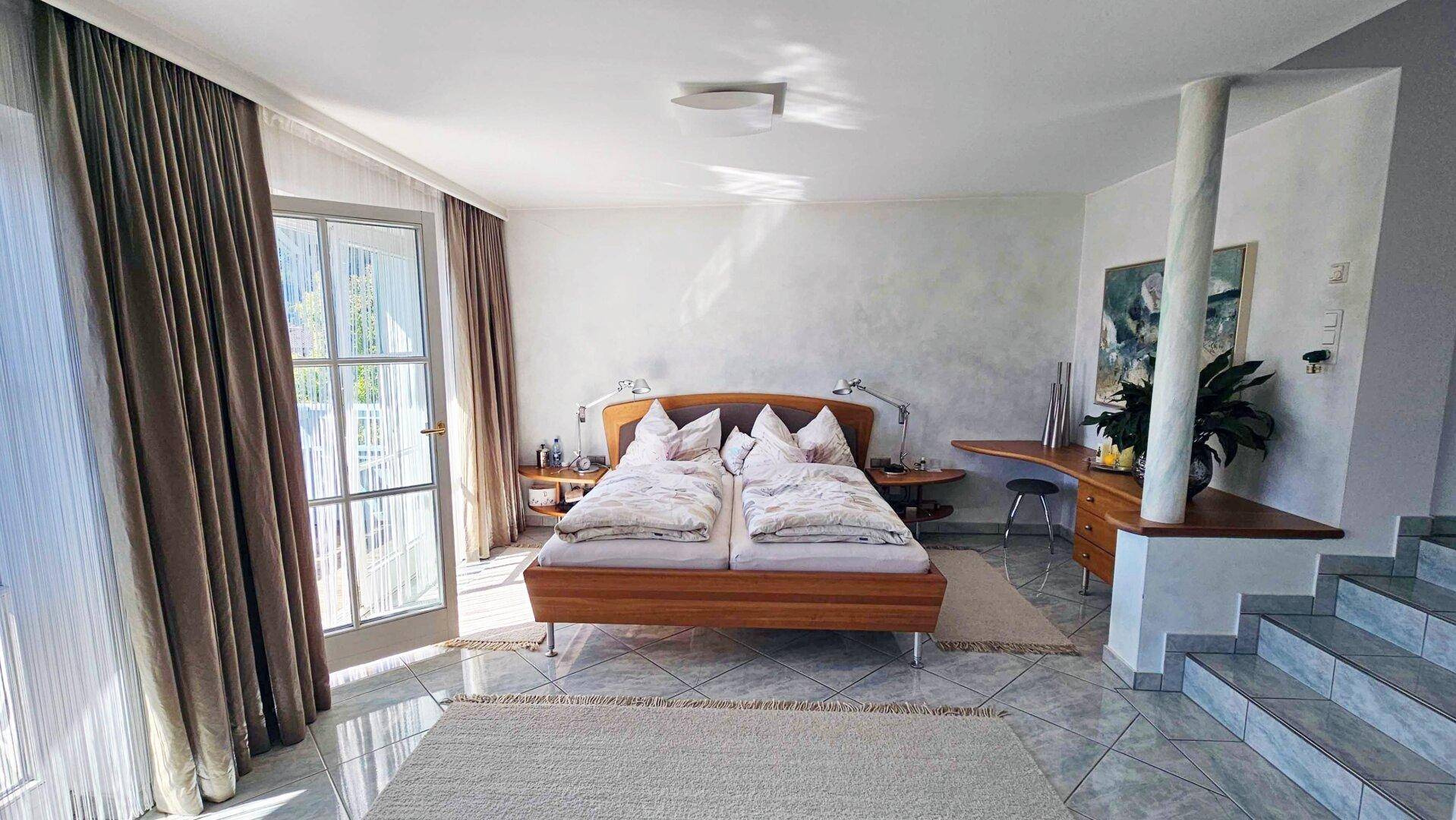 Helles Schlafzimmer mit Doppelbett, Fliesenboden und Zugang zu einem Balkon.