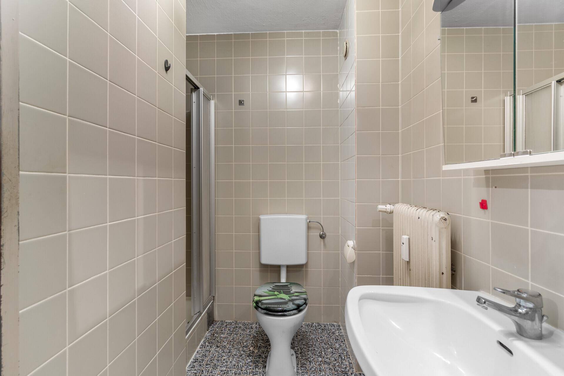 Badezimmer mit beigefarbenen Fliesen, WC, Waschbecken und Duschkabine.
