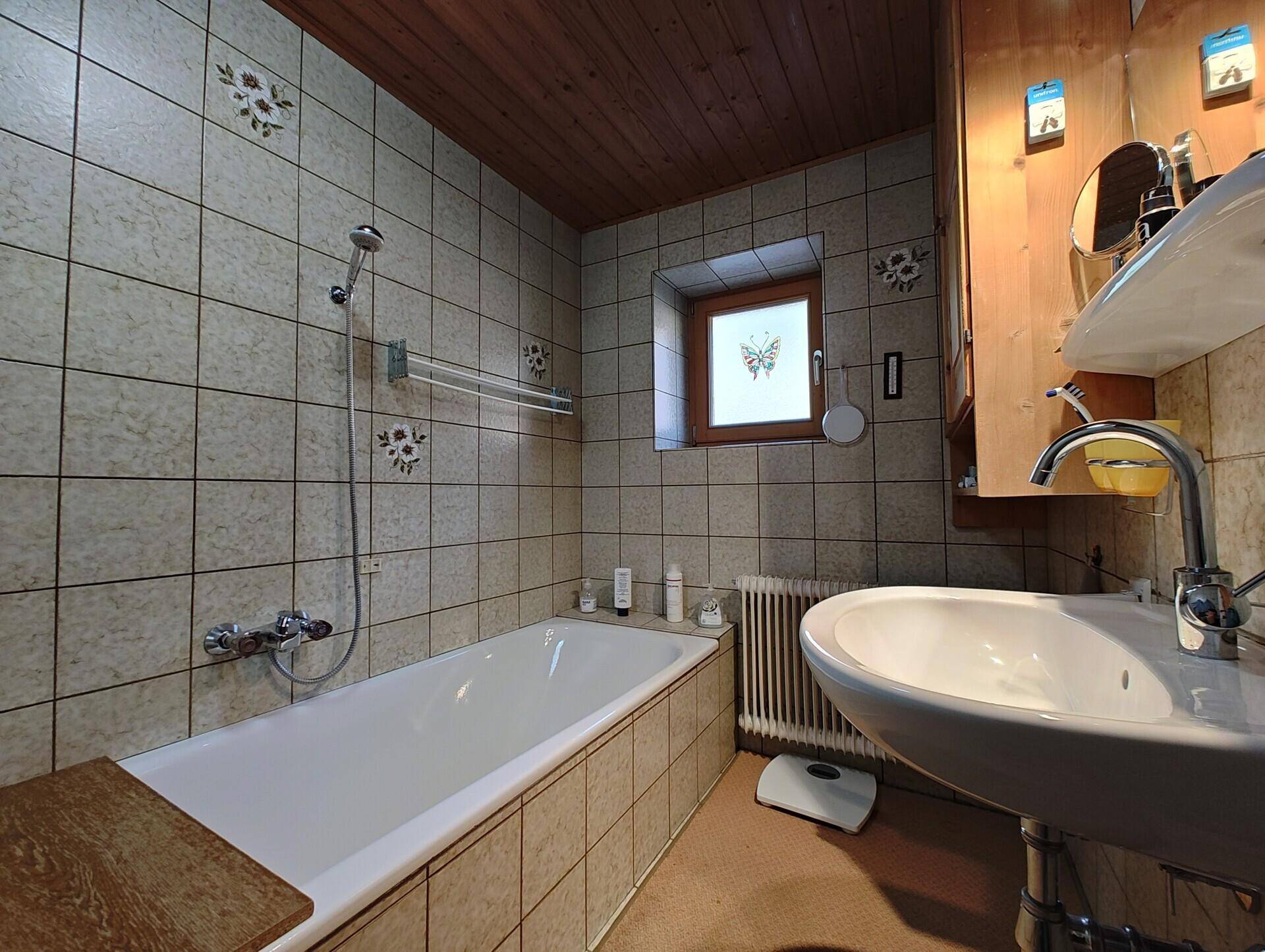 Badezimmer mit beigen Fliesen, Badewanne mit Duschfunktion und Holzdecke.