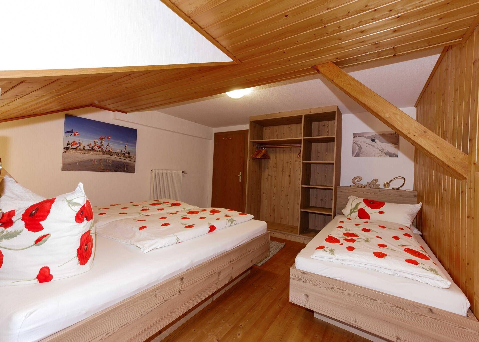 Gemütliches Schlafzimmer mit Holzbetten, Kleiderschrank und rustikaler Holzdecke.