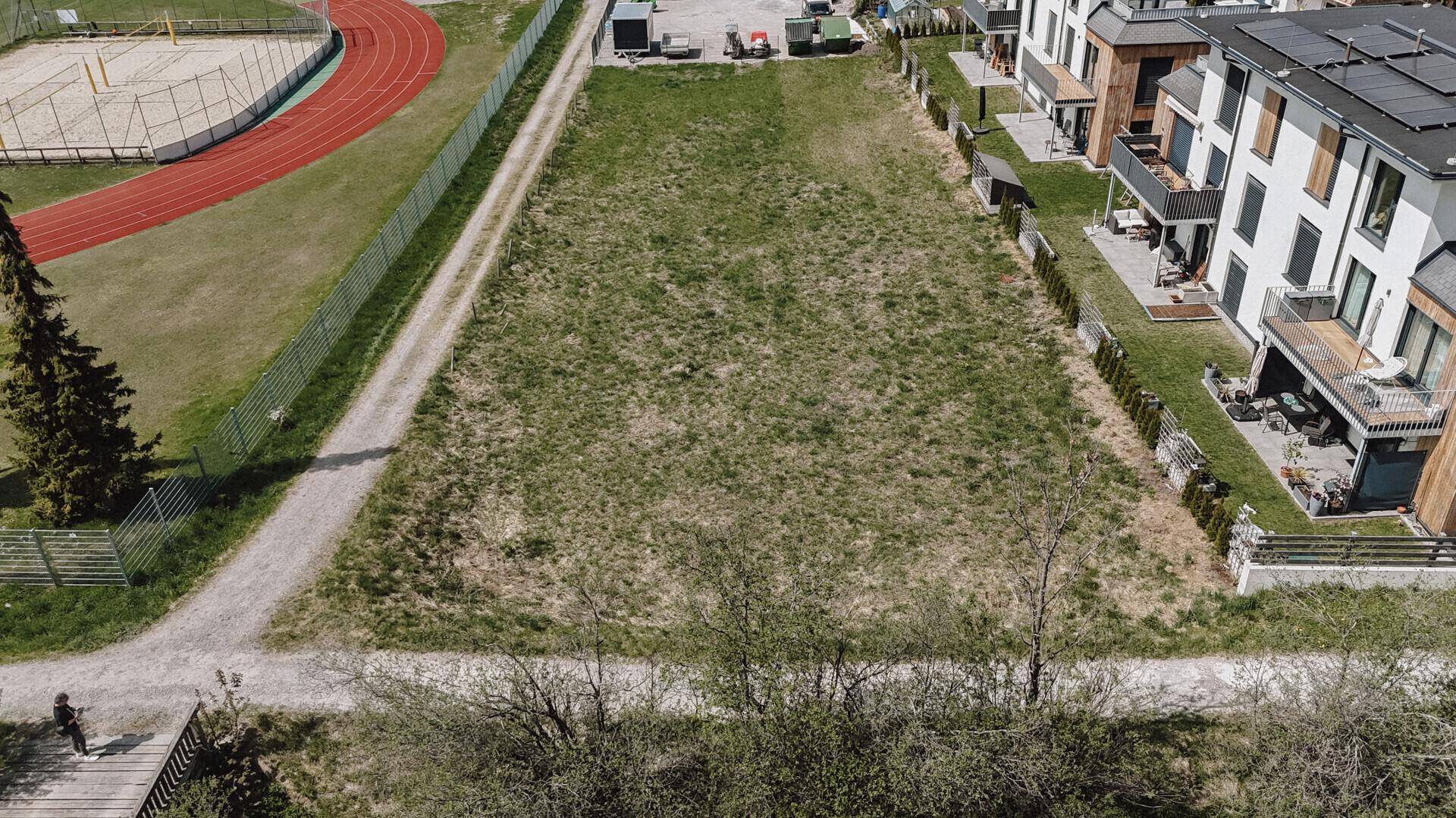 Weitläufiges grünes Grundstück mit einer Laufbahn und Bäumen im Hintergrund, angrenzend an moderne Wohngebäude.