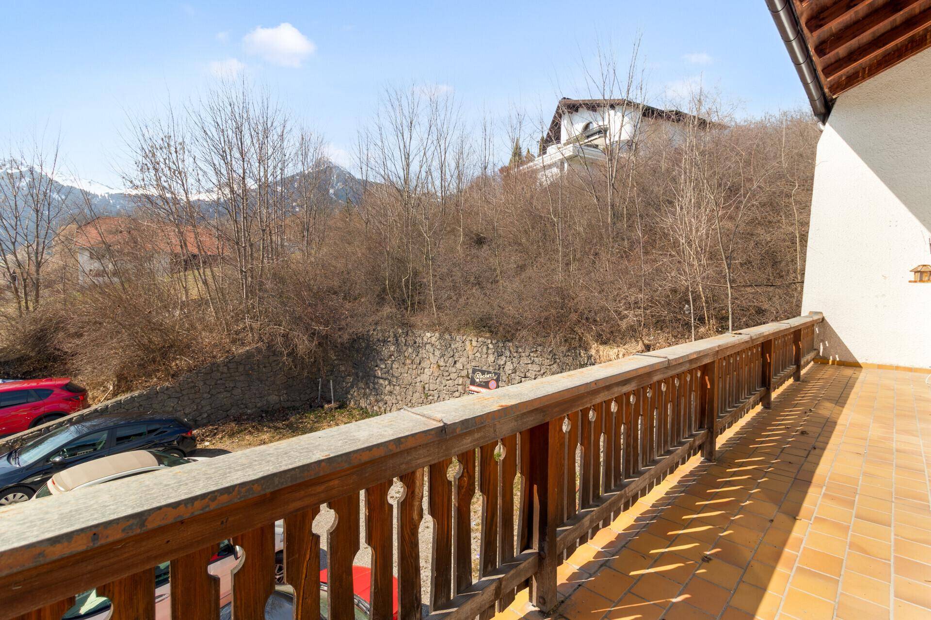 Geräumiger Balkon mit Fliesenboden, Holzgeländer und Blick auf die umliegende Natur und Berge.