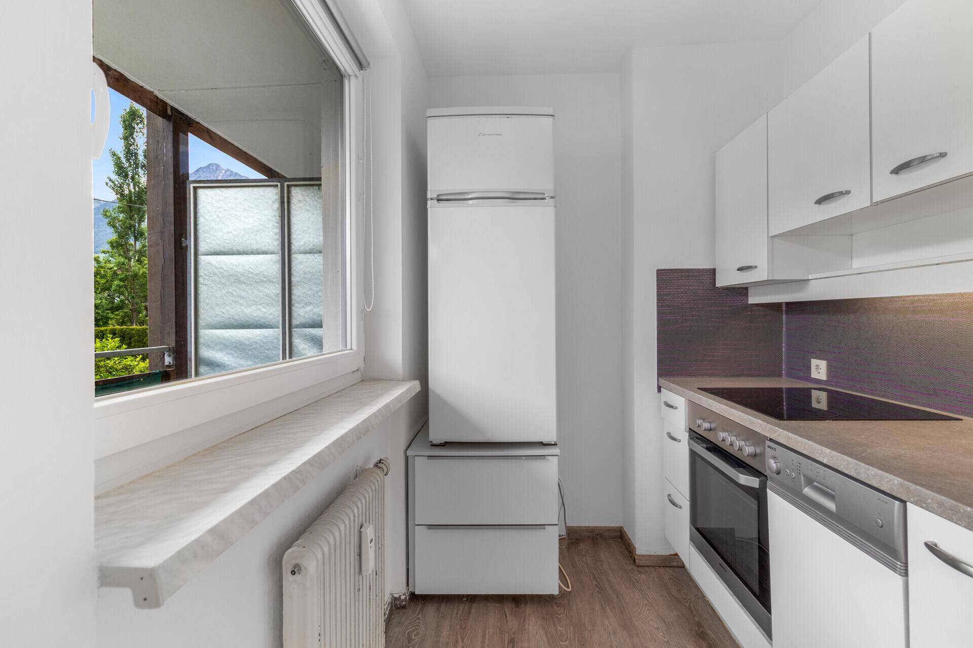Funktionale Küche mit weißen Schränken, modernen Geräten und Fenster mit Bergblick.