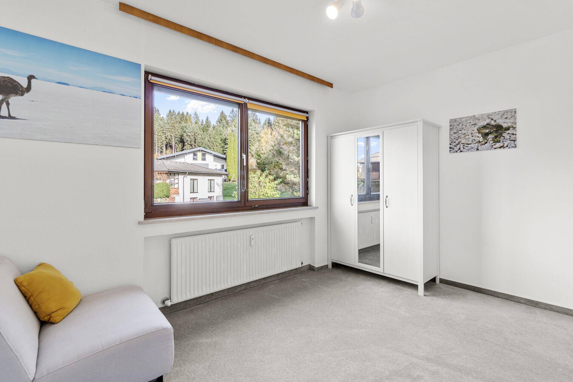 Freundliches Schlafzimmer mit Fenster und Blick auf die Umgebung, ausgestattet mit einem Kleiderschrank und Sofa.