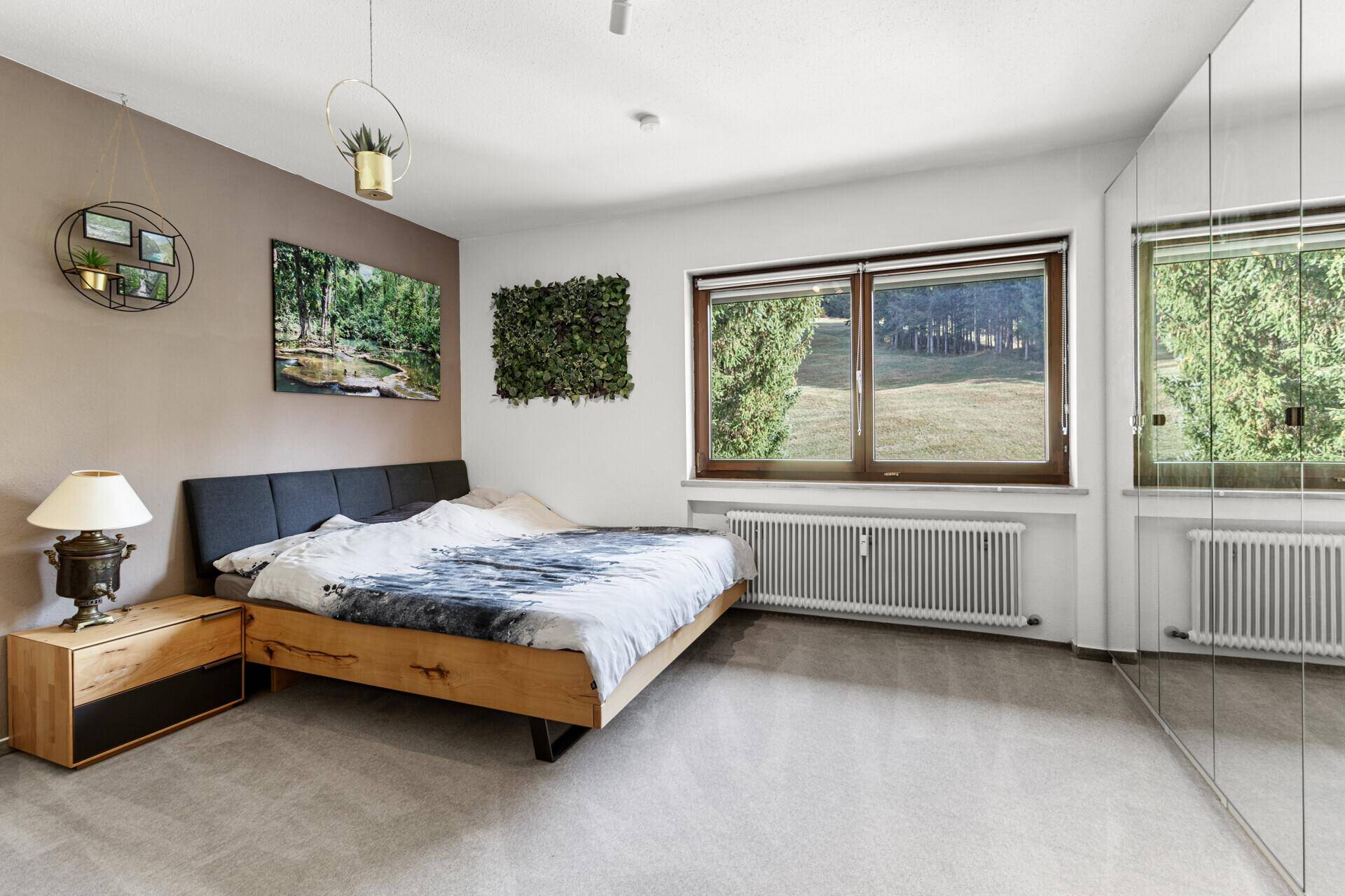 Helles Schlafzimmer mit großem Fenster und Blick ins Grüne, ausgestattet mit einem modernen Bett und Spiegelschränken.