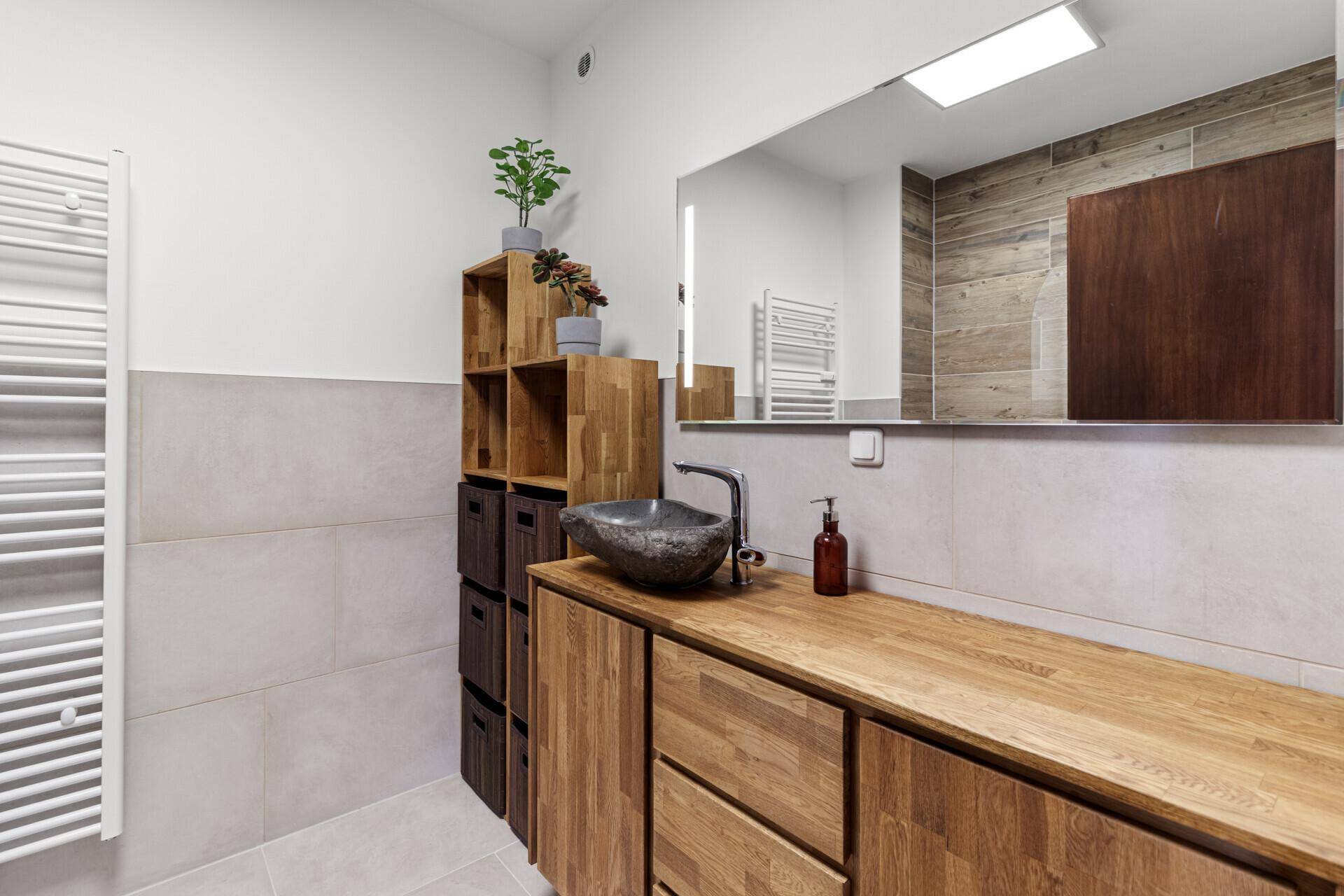 Modernes Badezimmer mit stilvollem Holzwaschtisch, Steinsink und großem Spiegel, der den Raum aufhellt.