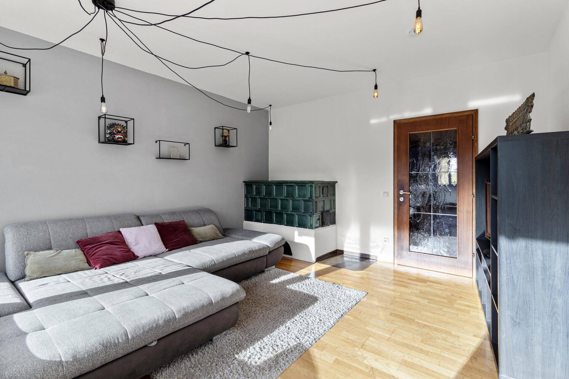 Gemütliches Wohnzimmer mit modernem Sofa, traditionellem Kachelofen und Holzboden, ideal zum Entspannen.