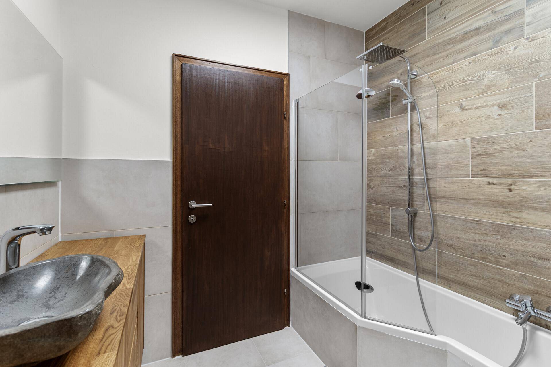 Modernes Badezimmer mit Badewanne und Duschkombination, sowie eleganten Holzoptik-Fliesen an den Wänden.