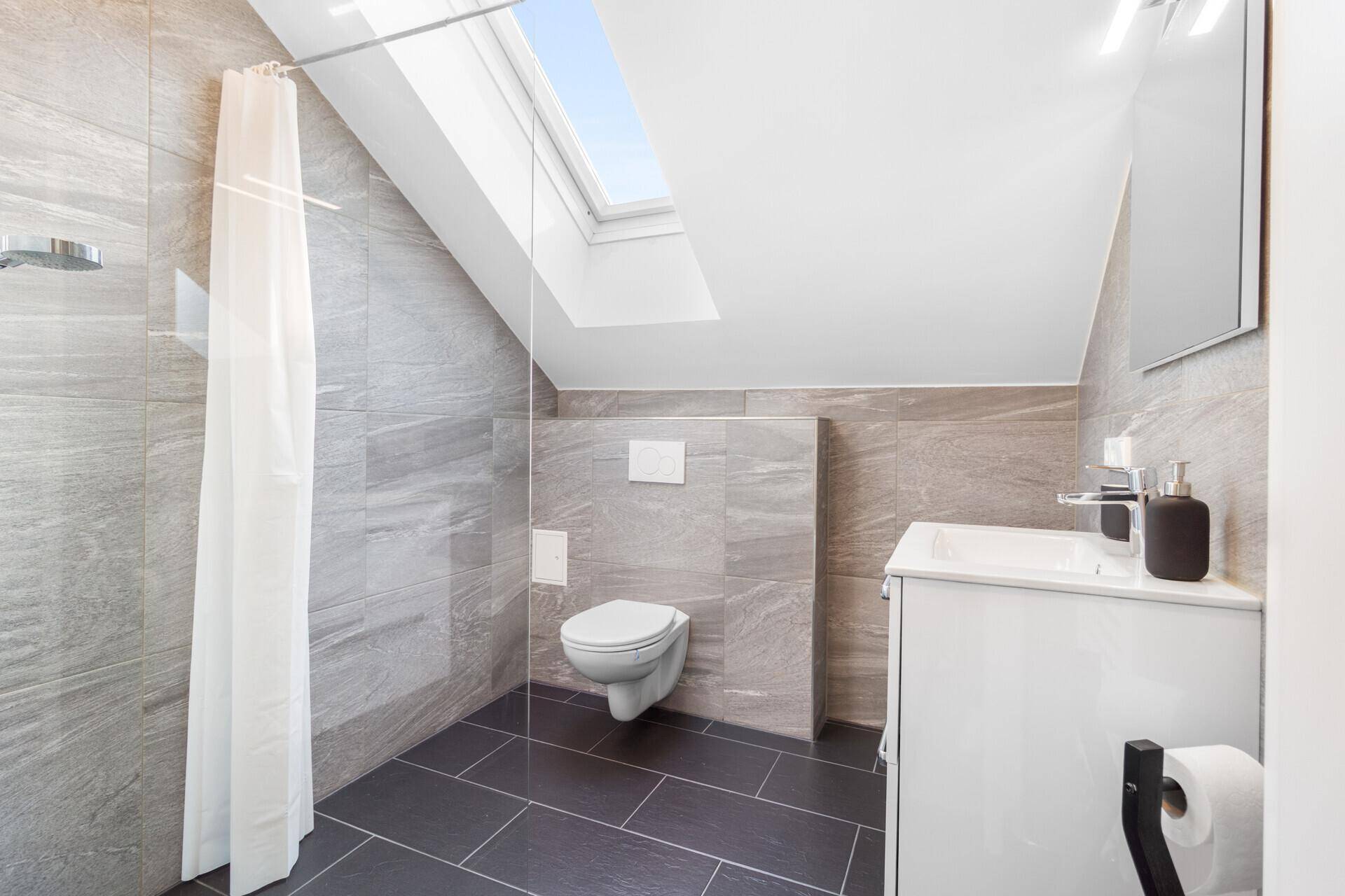Modernes Badezimmer mit Dusche, Wand-WC, Waschtisch und Dachfenster im Dachgeschoss.