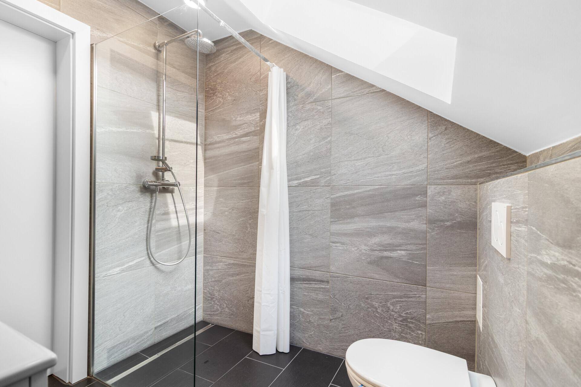 Duschbereich im modernen Badezimmer mit grauen Fliesen und Wand-WC.