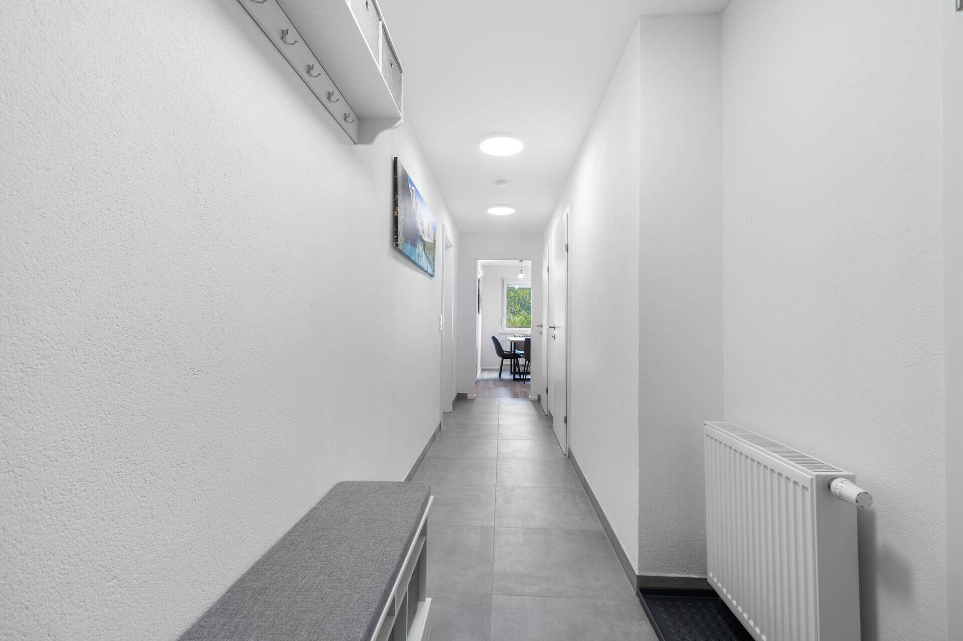 Langer, heller Flur mit Fliesenboden, Heizkörper und Blick in den Wohnbereich.