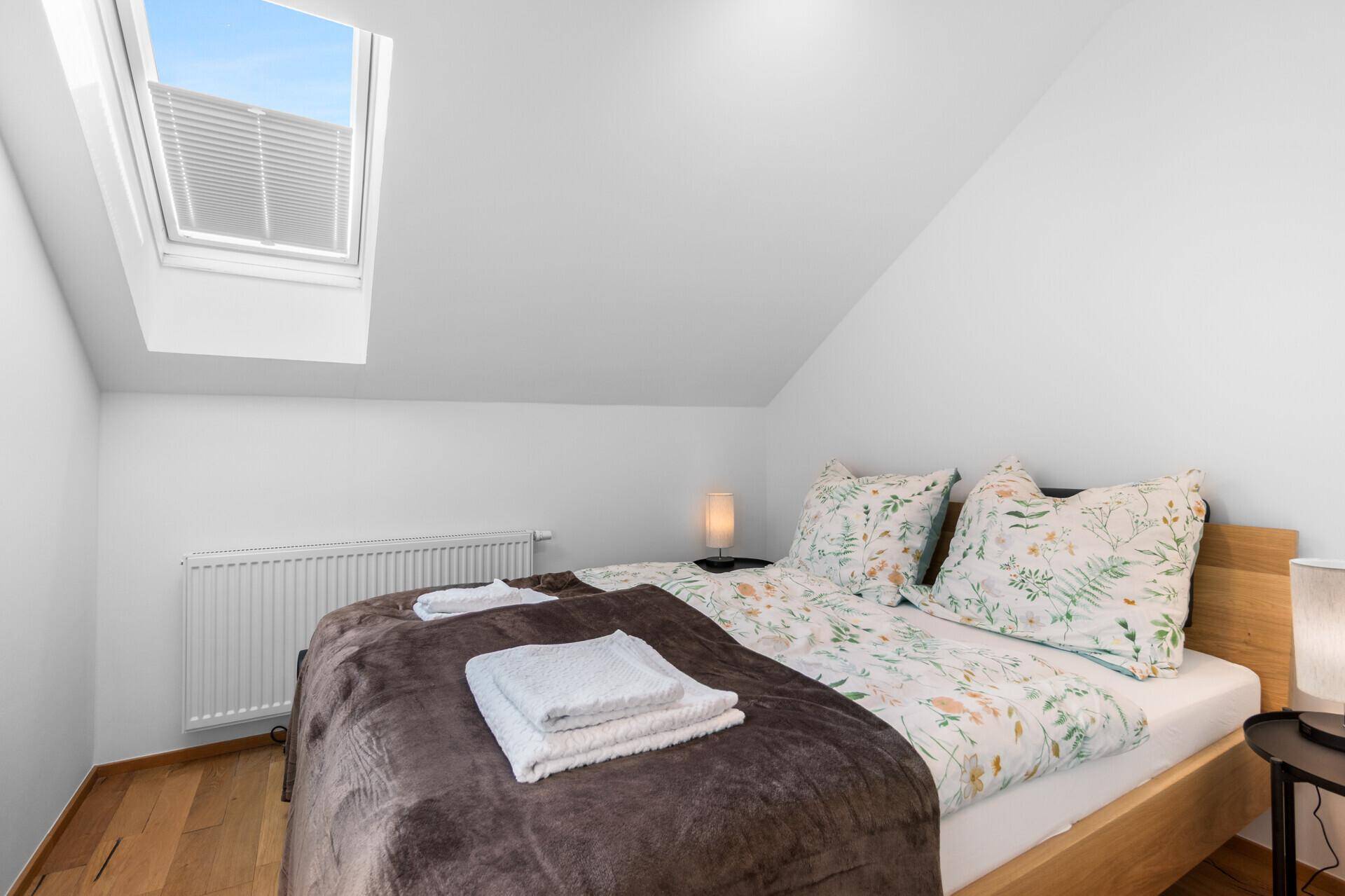 Schlafzimmer im Dachgeschoss mit Holzbett, Dachfenster und heller, freundlicher Atmosphäre.