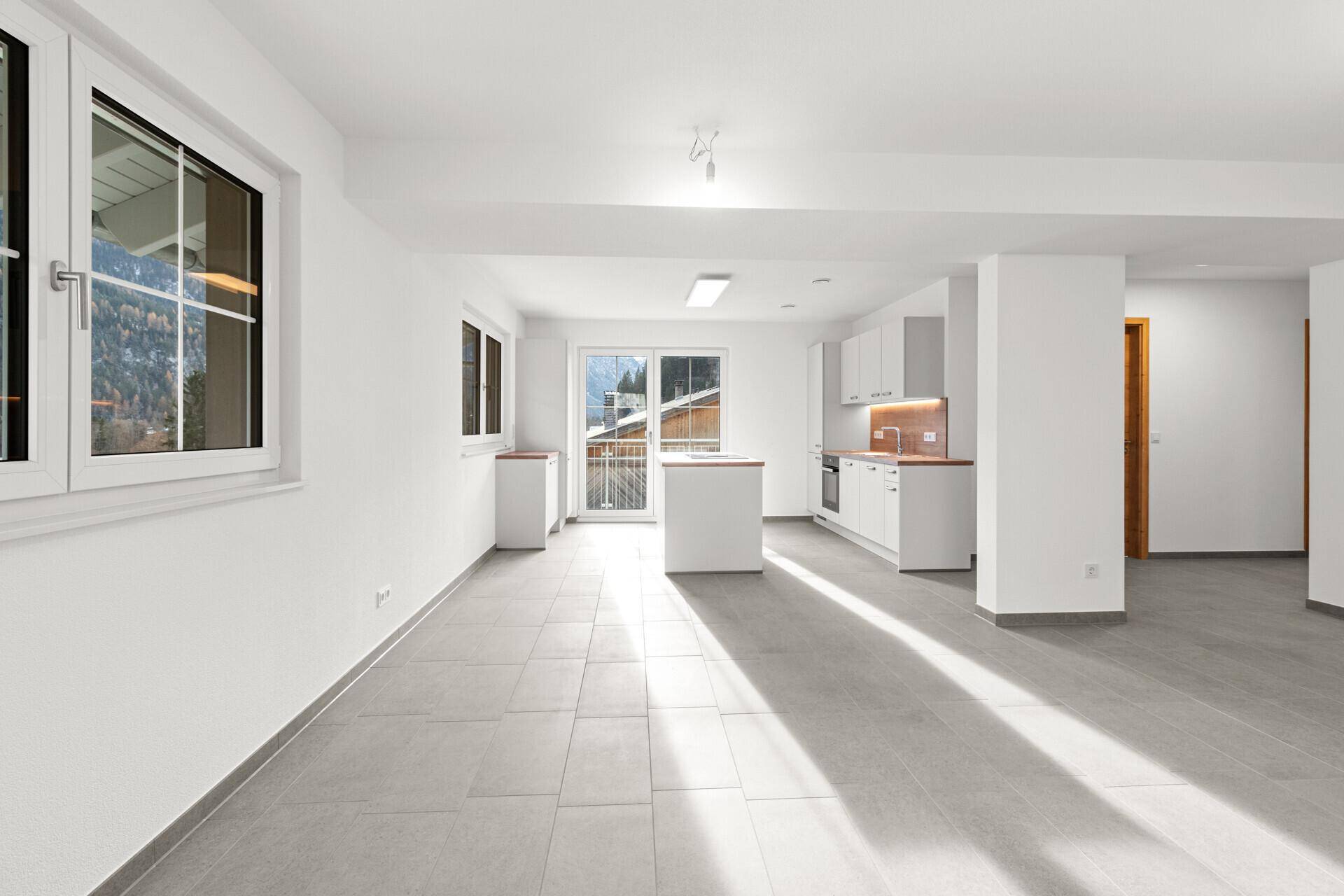 Heller, offener Wohnbereich mit Fliesenboden und Zugang zum Balkon mit Bergblick.