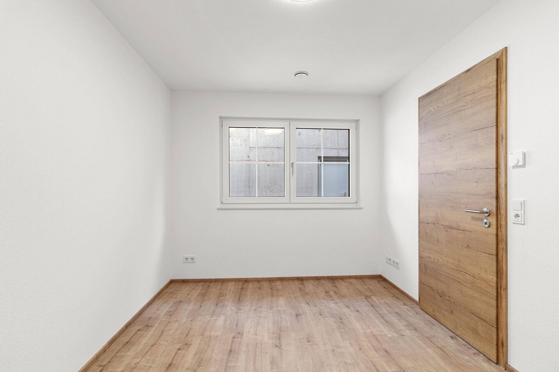 Leeres Zimmer mit Laminatboden und Fenster, ideal als Schlaf- oder Arbeitszimmer nutzbar.