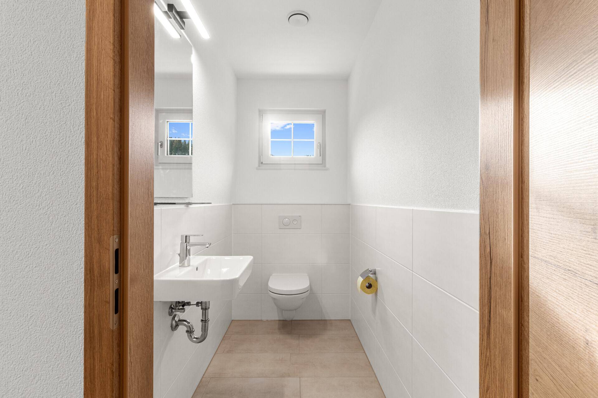 Separates Gäste-WC mit Fenster, Waschbecken und modernen Armaturen in hellem Design.