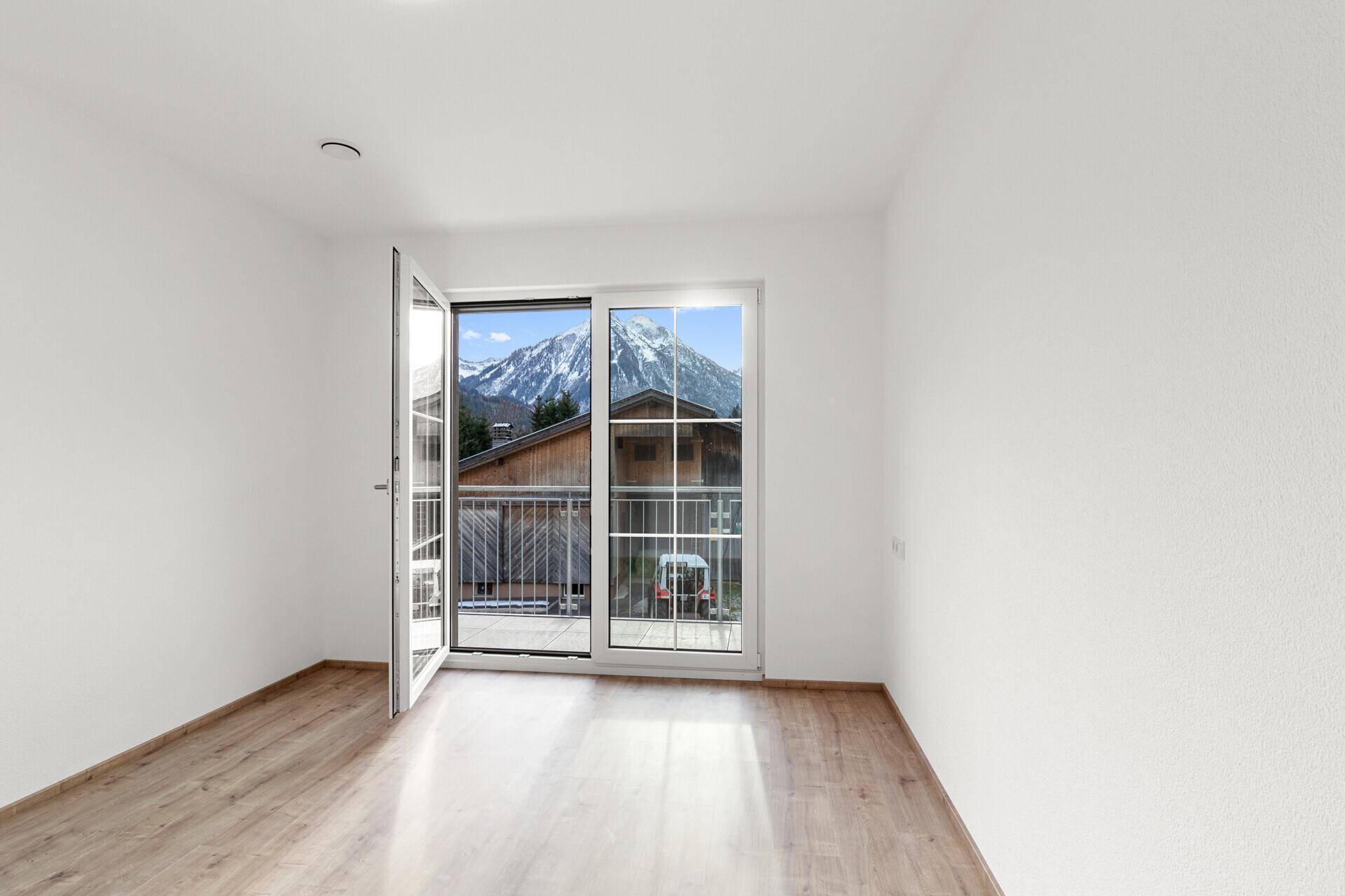 Helles Zimmer mit Laminatboden, Balkonzugang und beeindruckendem Bergblick.