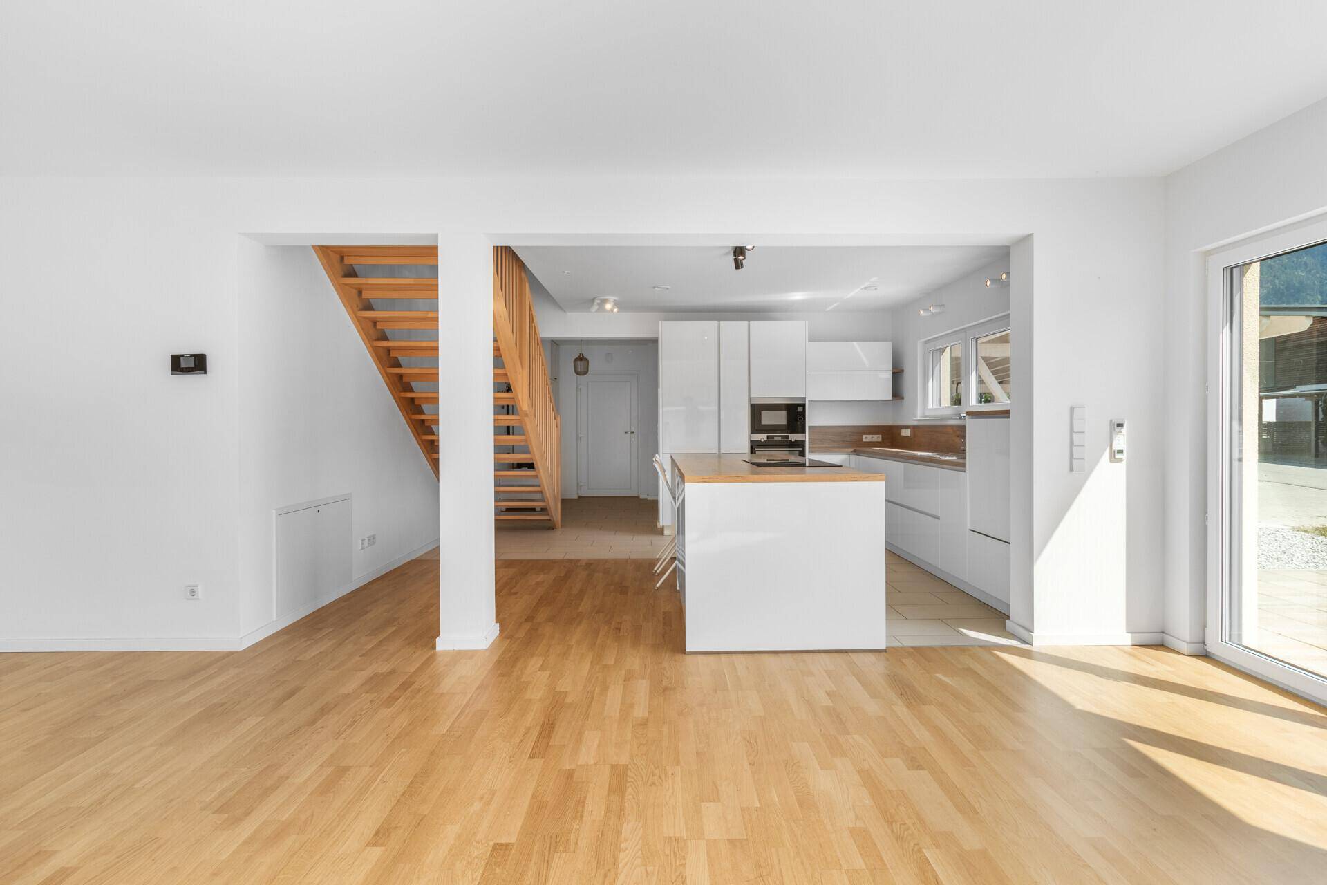 Offener Wohnbereich mit Holzboden, weißer Küche und Treppe zum Obergeschoss.