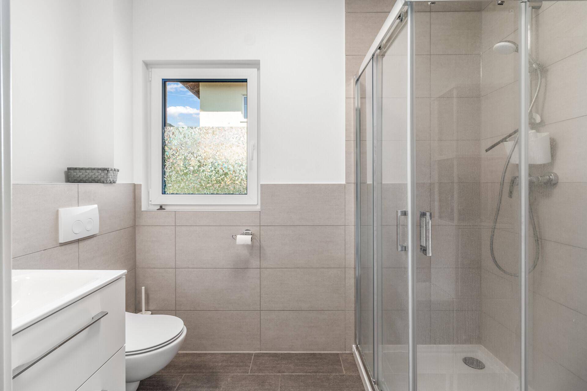Modernes Badezimmer mit Dusche, WC und Fenster.