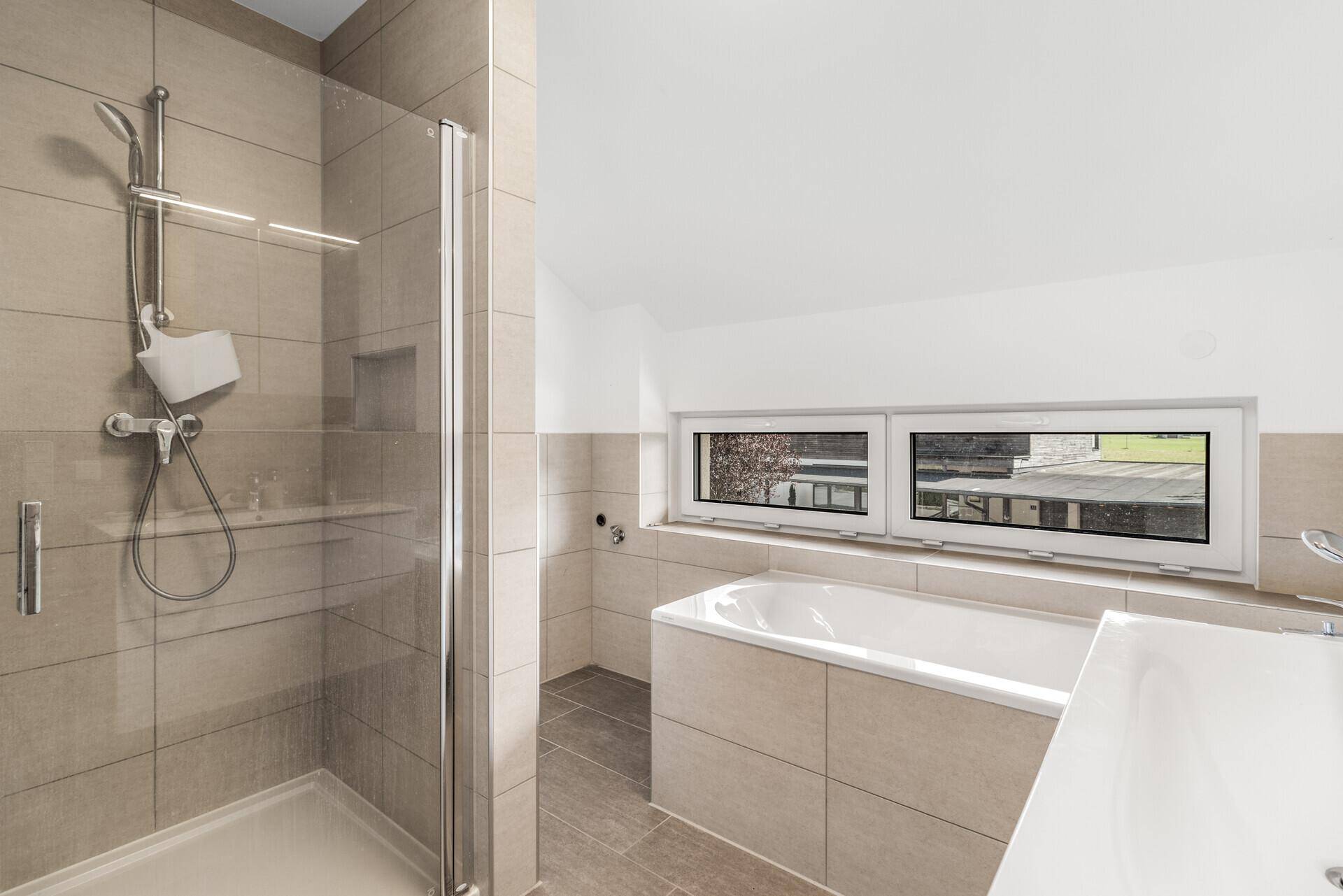 Modernes Badezimmer im Dachgeschoss mit Badewanne, Dusche und Fenster.