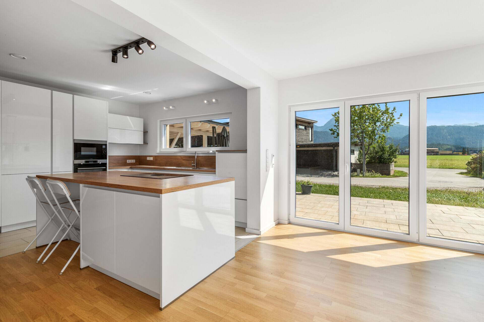Moderne weiße Küche mit Kochinsel, Holzarbeitsplatte und Zugang zur Terrasse.