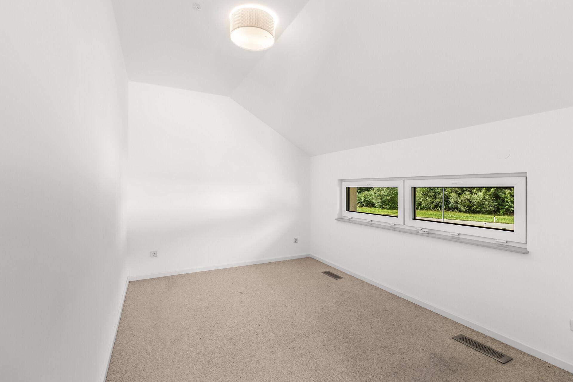 Helles Schlafzimmer im Dachgeschoss mit Teppichboden und Blick ins Grüne.