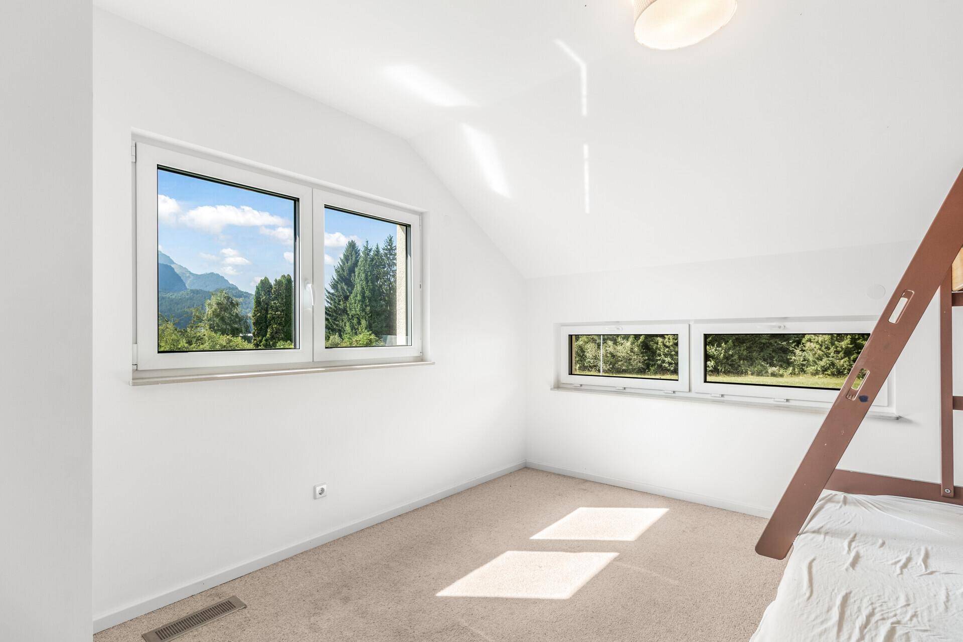 Helles Schlafzimmer im Dachgeschoss mit Teppichboden und Bergblick.