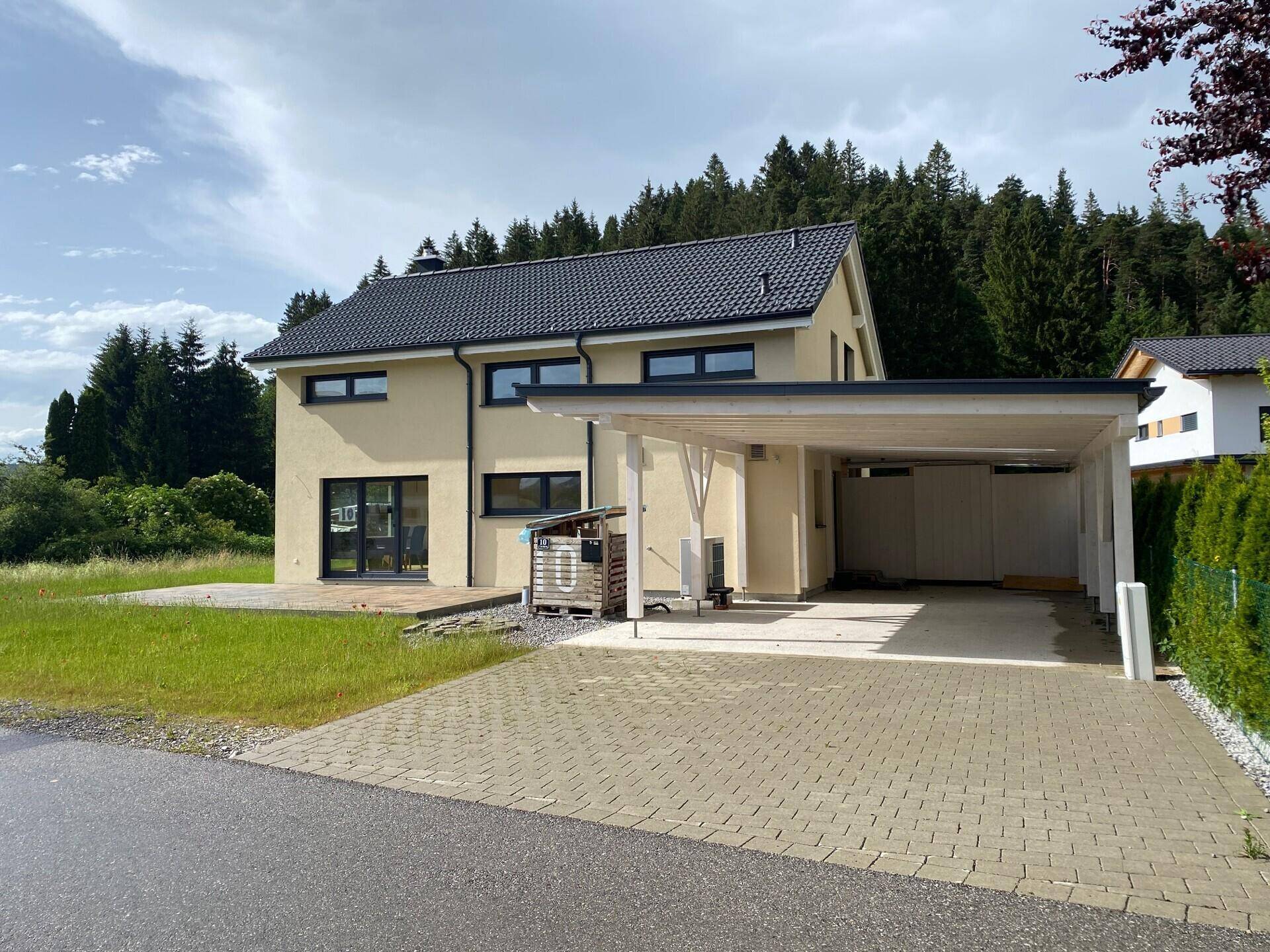 Modernes Einfamilienhaus mit Carport und gepflasterter Zufahrt in ländlicher Umgebung.