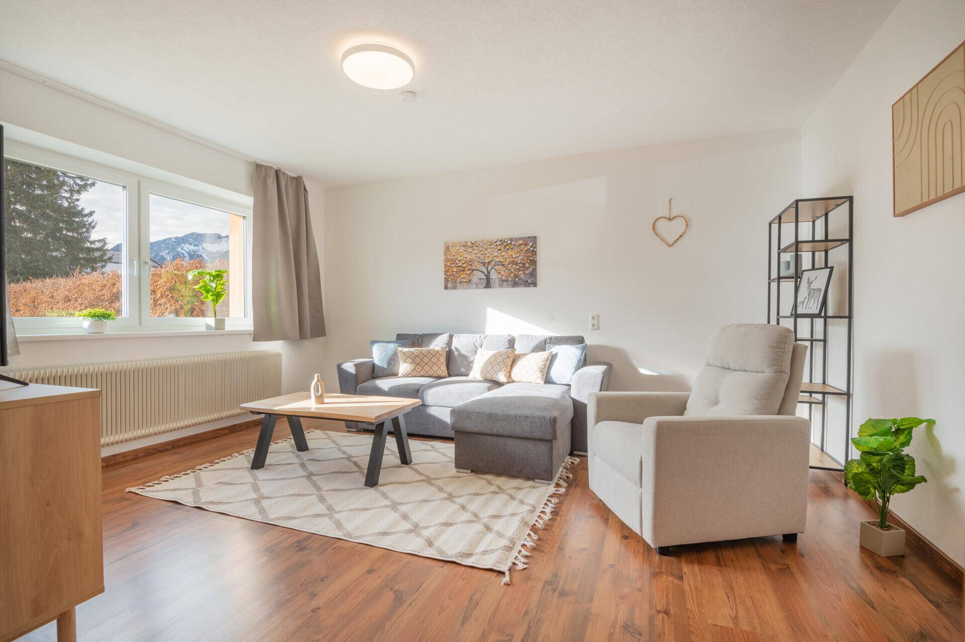 Gemütliches Wohnzimmer mit Holzboden, modernem Sofa und Blick auf die Berge.
