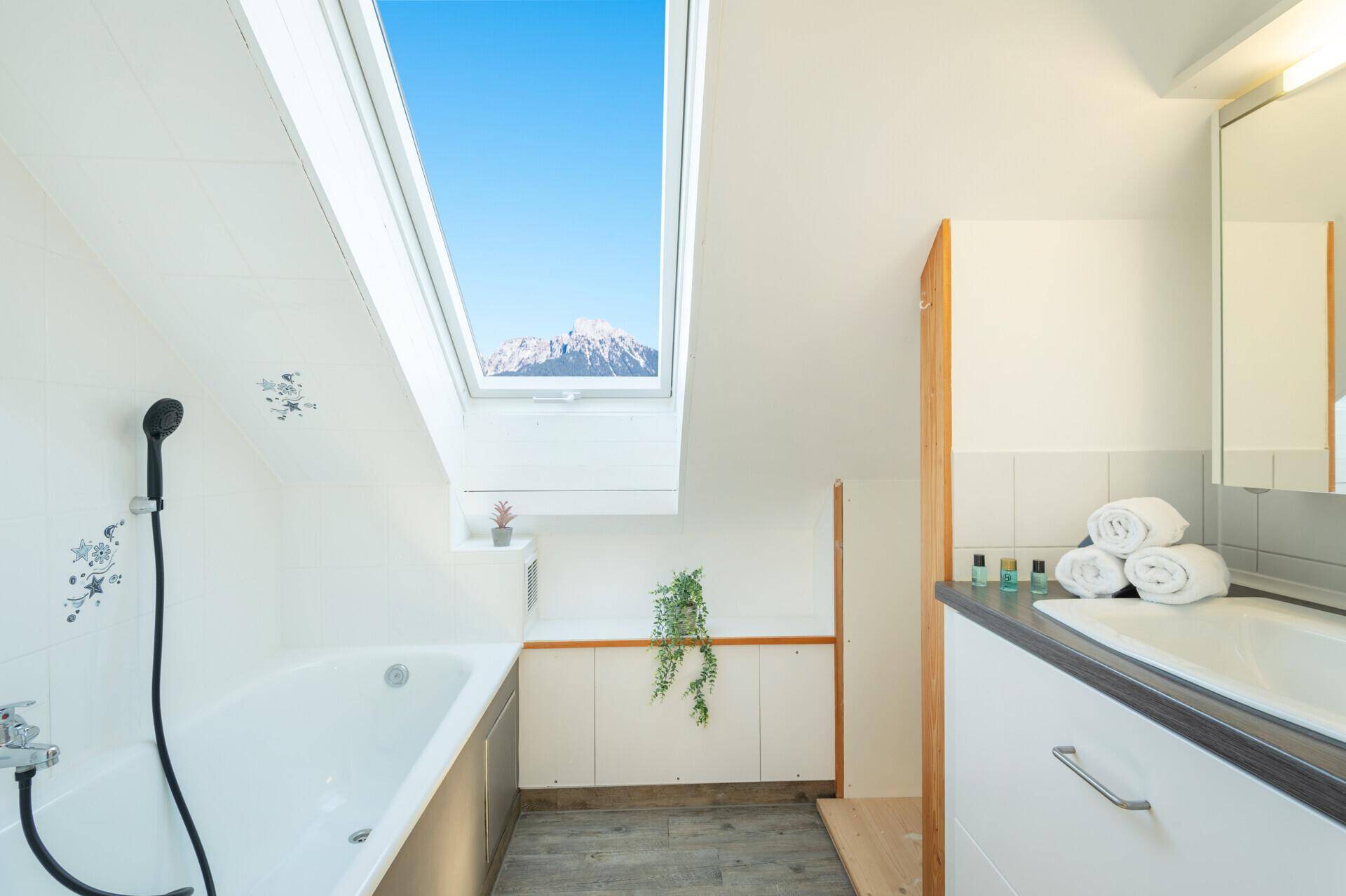 Helles Dachgeschoss-Badezimmer mit Badewanne, Dachfenster und Bergblick.